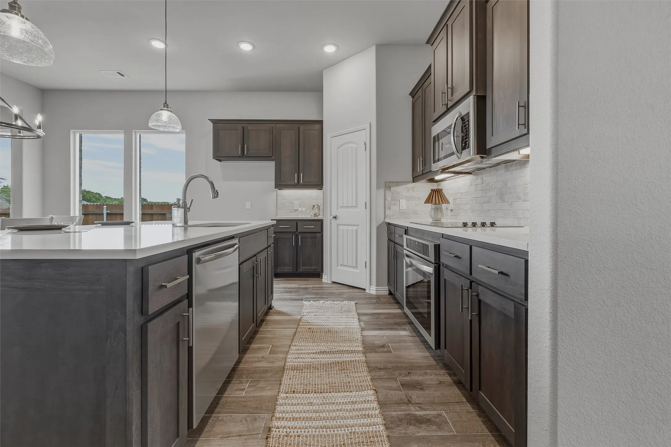 Stainless steel appliances, wood-finish flooring, white countertops, built-in microwave, and pendant lighting