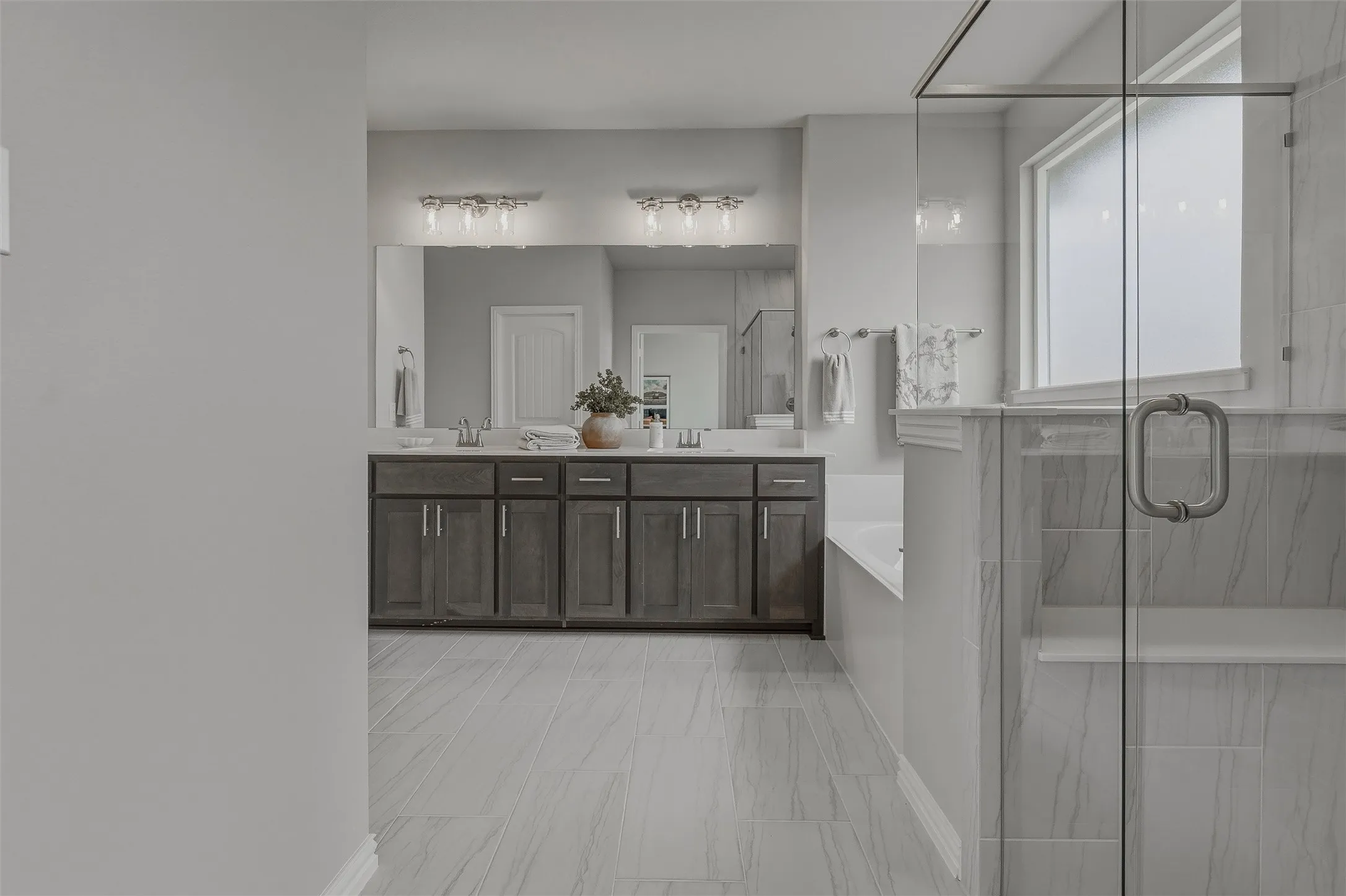 Dual vanity with dark wood-finish cabinetry, built-in soaking tub, glass-enclosed shower, and large frosted window