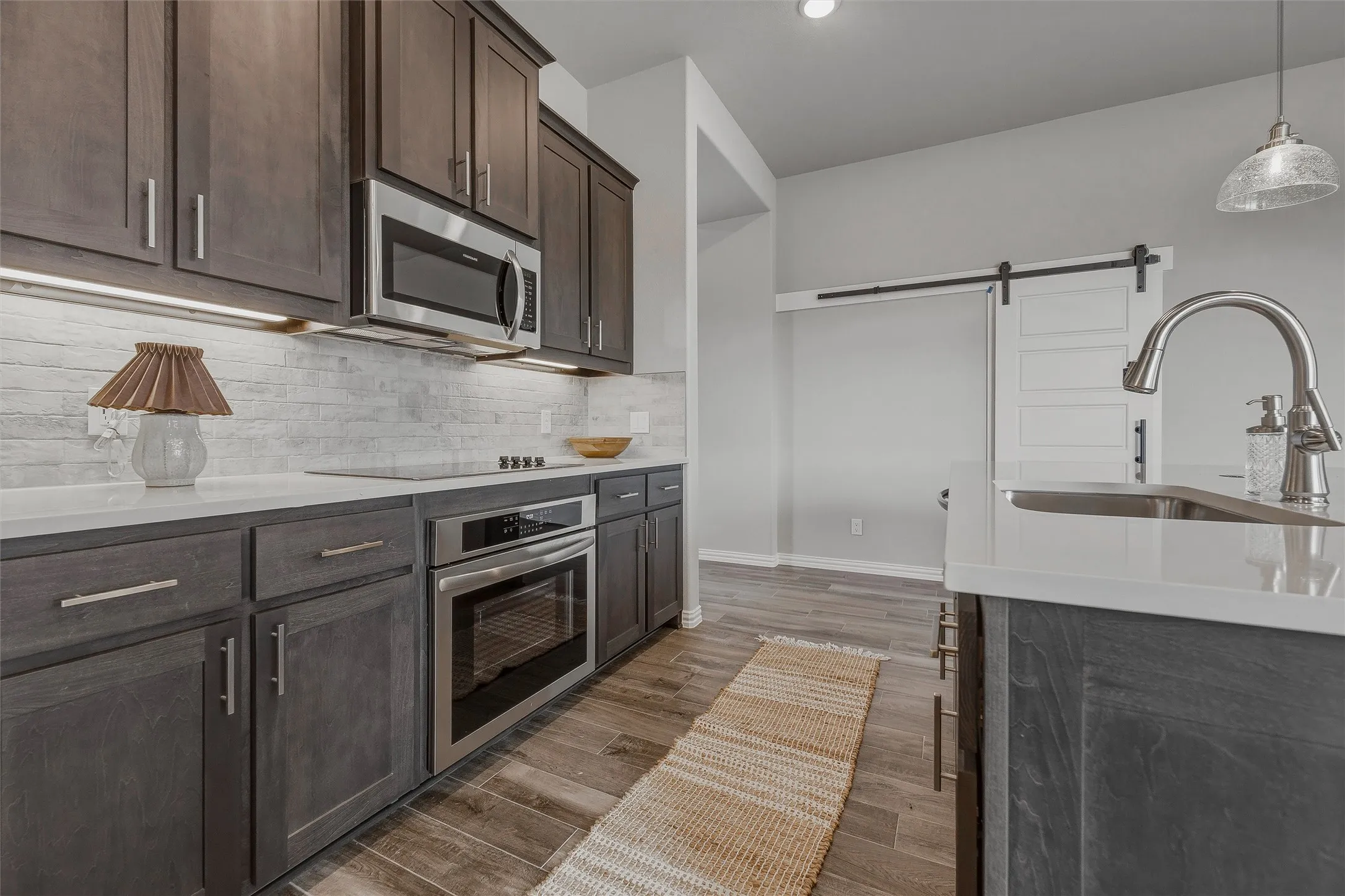 Kitchen featuring wood-finish flooring, dark wood cabinetry, white countertops, stainless steel appliances, and a white barn door