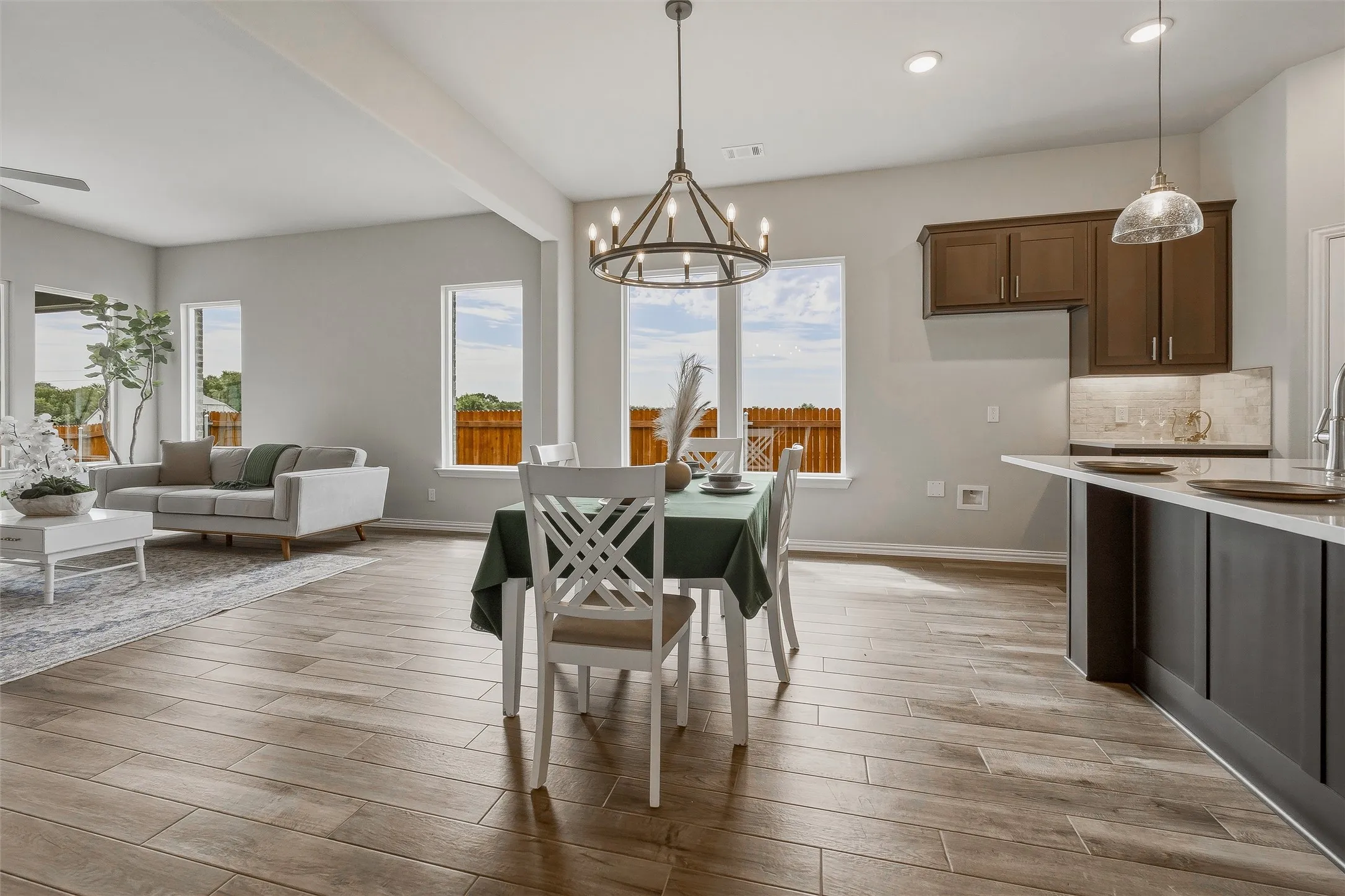 Wood-finish flooring throughout, framed windows, contemporary chandelier, kitchen island with counter seating, and dark wood cabinetry