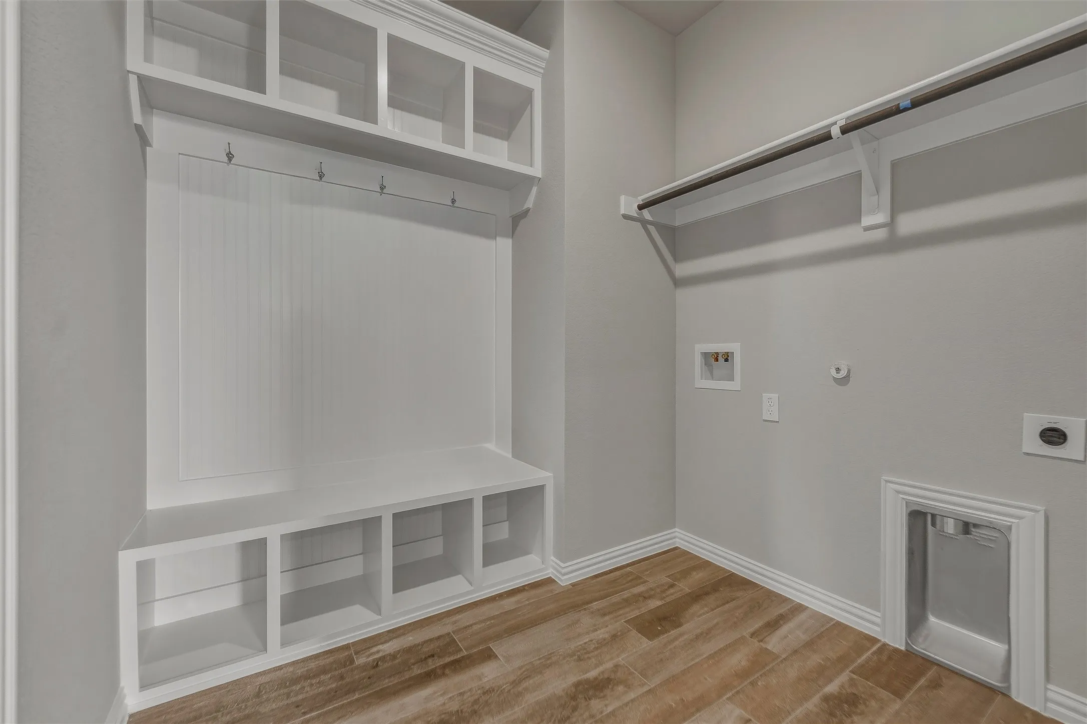 Utility area featuring wood-finish flooring, built-in mudroom storage with integrated bench and hooks, white painted cabinetry, and a laundry hookup