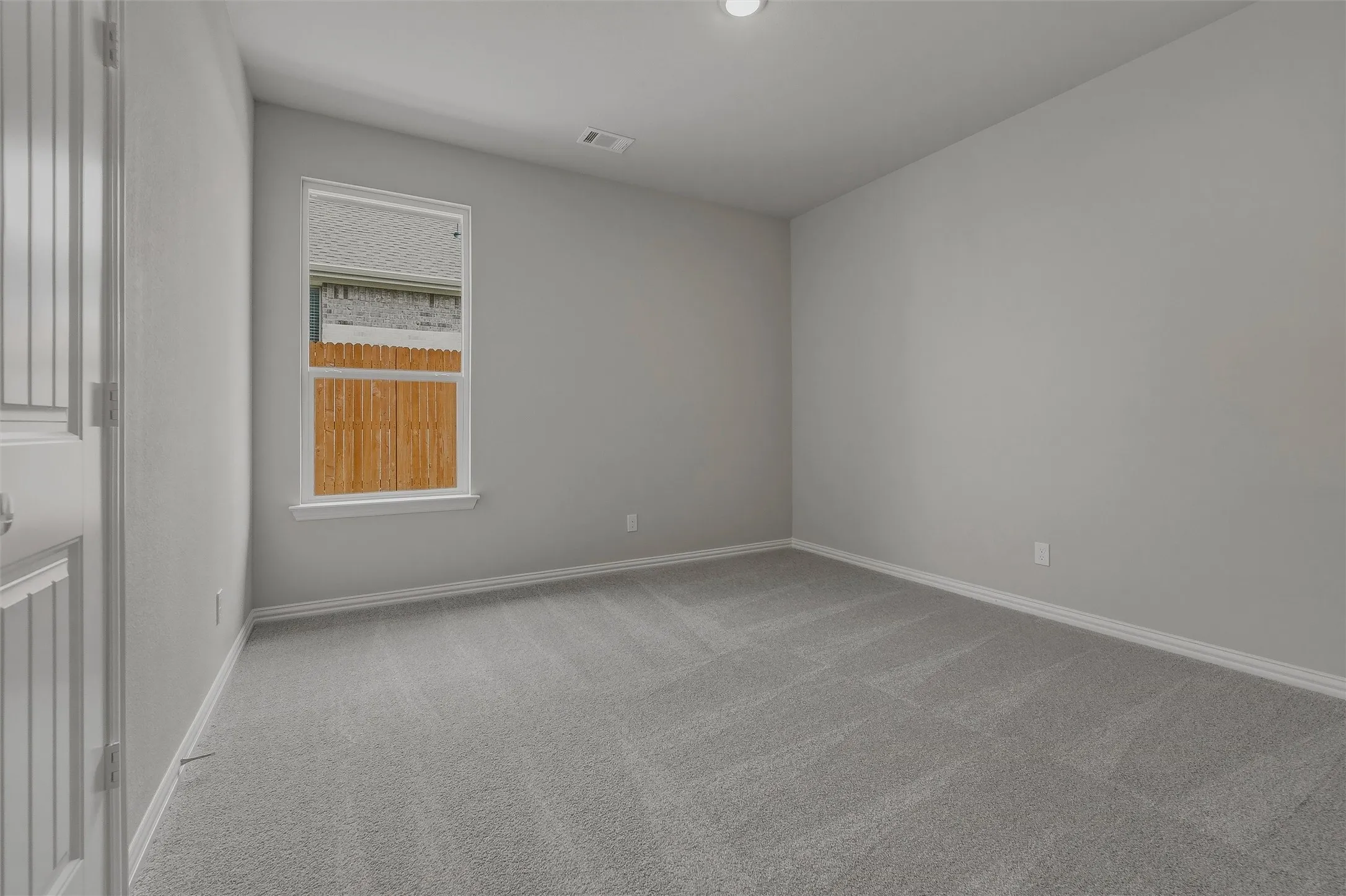 Neutral gray wall paint, gray carpeting, white trim, recessed ceiling light, and a window with white framing