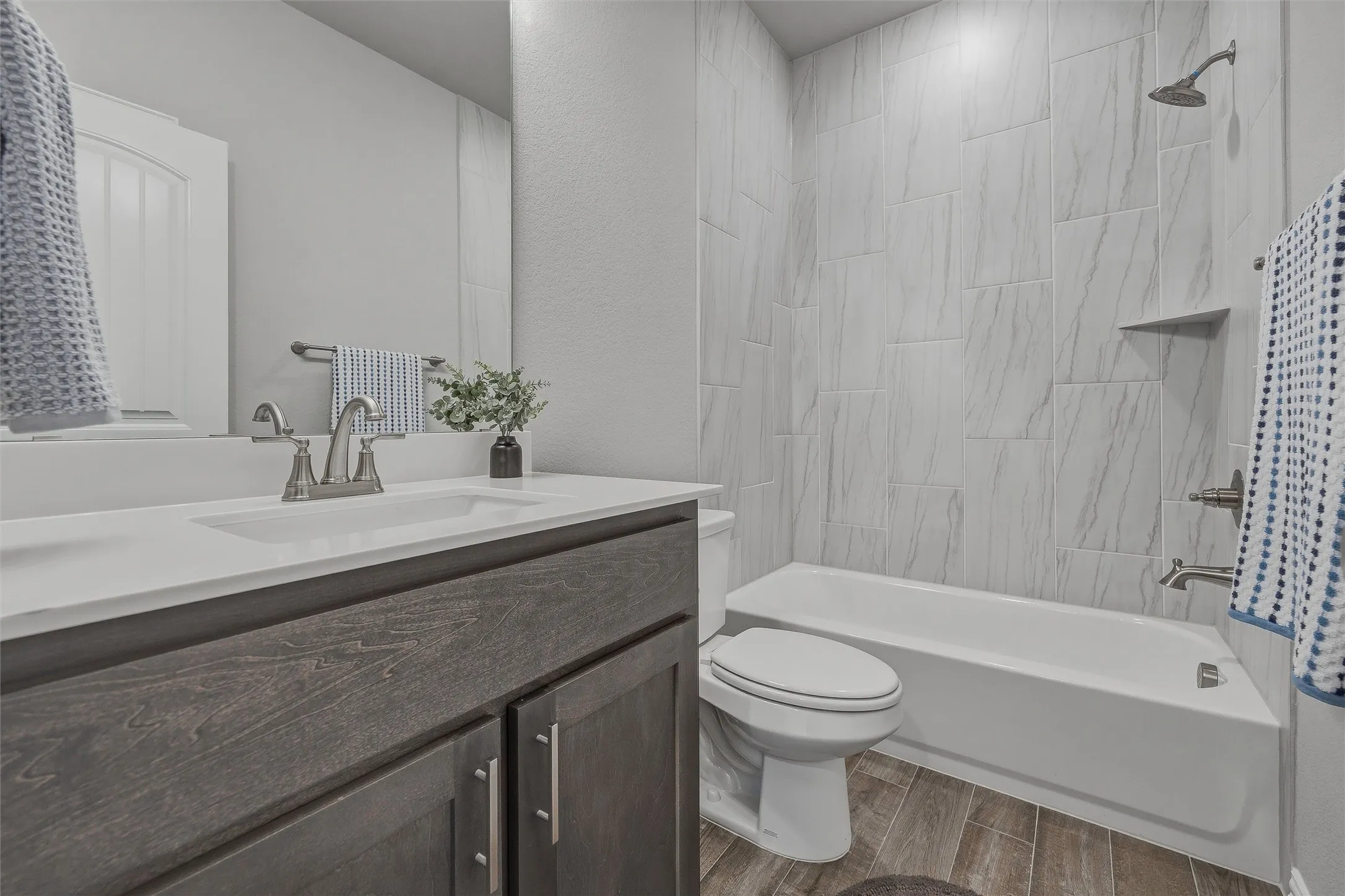 Bathroom featuring a wood-finish vanity with an integrated sink, brushed nickel faucet, a combination shower and tub with full-height tile surround, and wood-look flooring