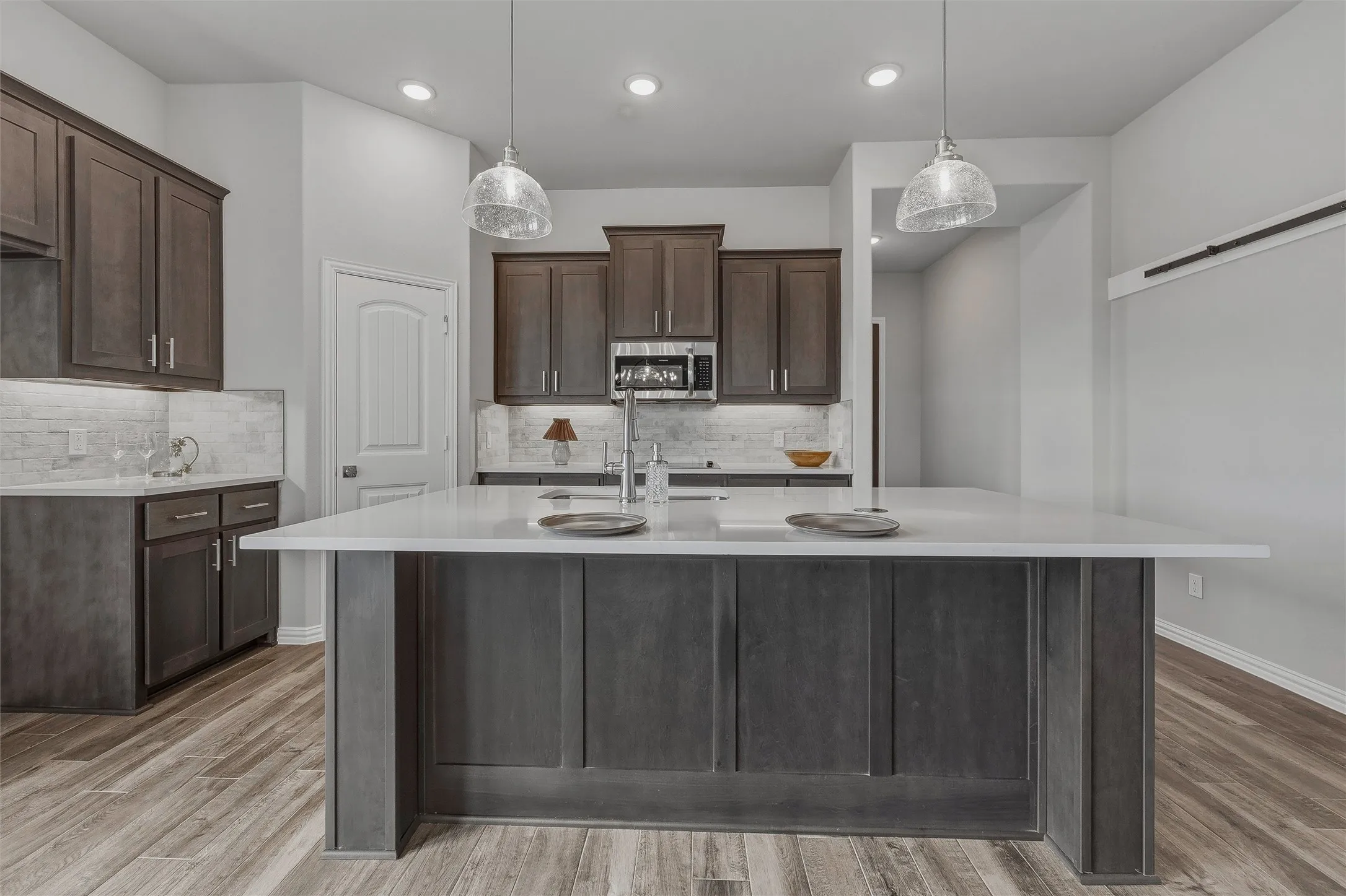 Kitchen featuring a center island with a white countertop, dark wood-finish cabinetry, wood-finish flooring, and pendant lighting