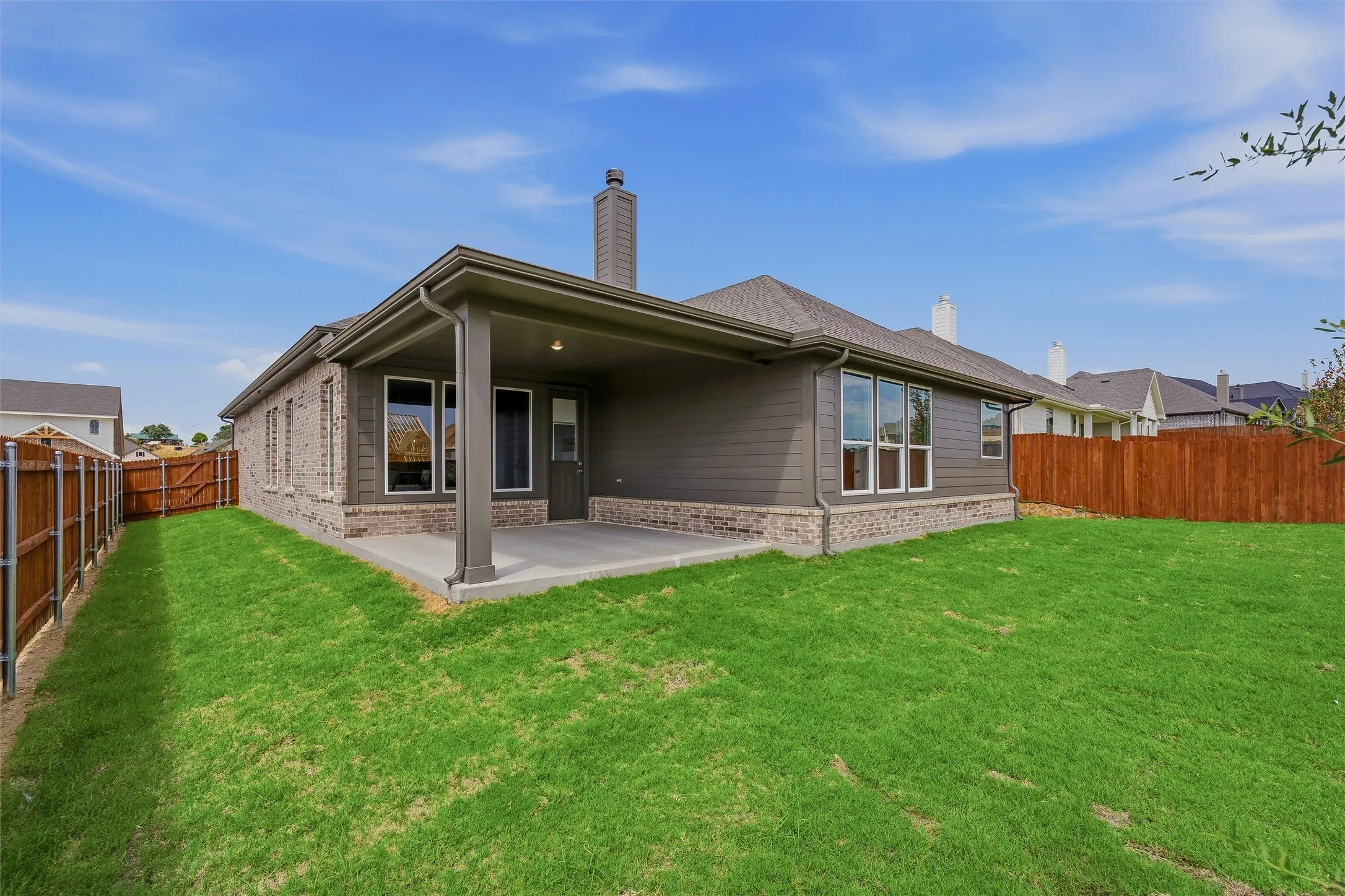 Expansive grass lawn with a covered concrete patio, brick and siding exterior, and a wood privacy fence