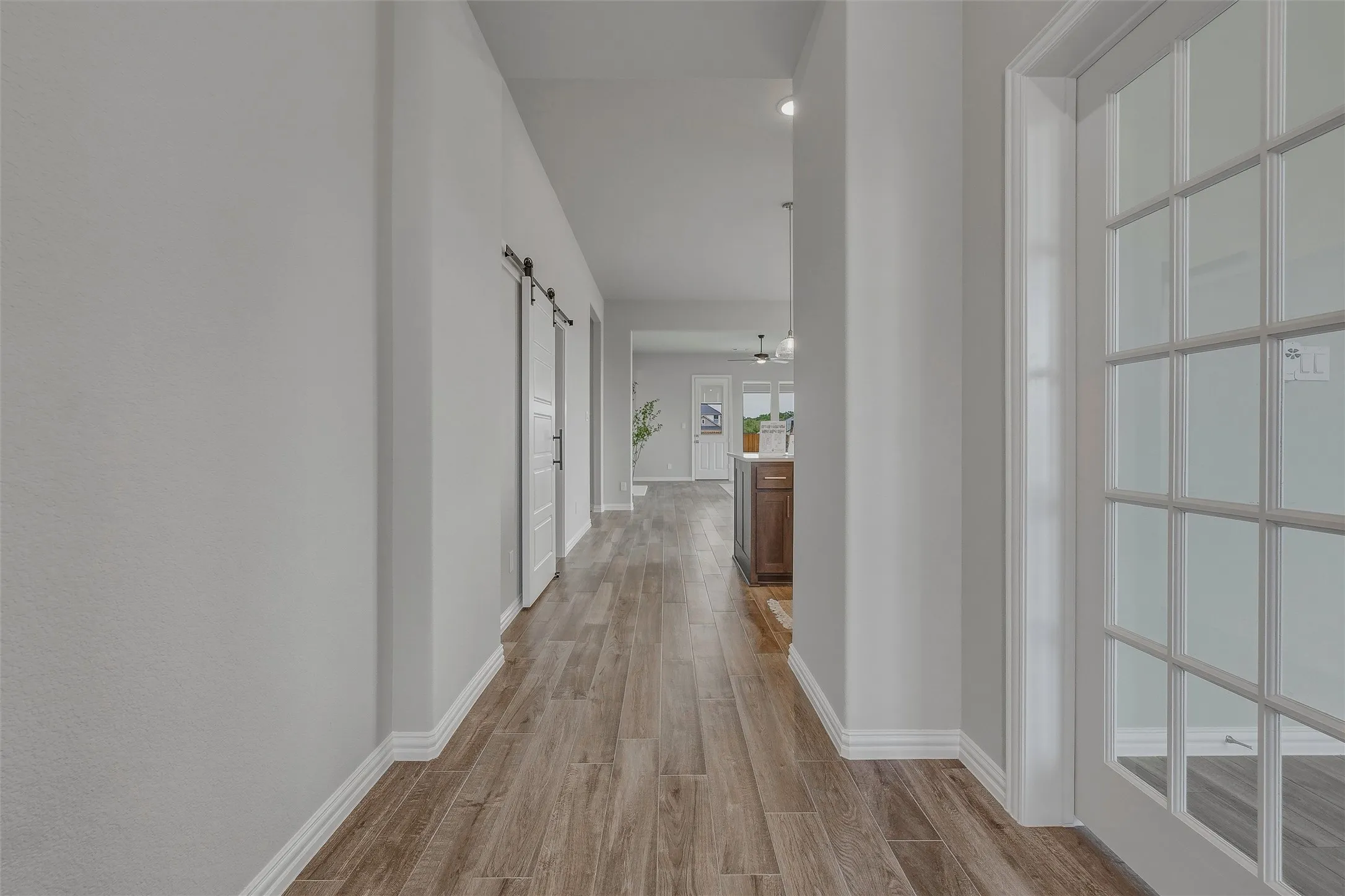 Wood-finish flooring extending through the hallway, white interior walls, white paneled barn doors with black hardware, and a white French door with multiple lites
