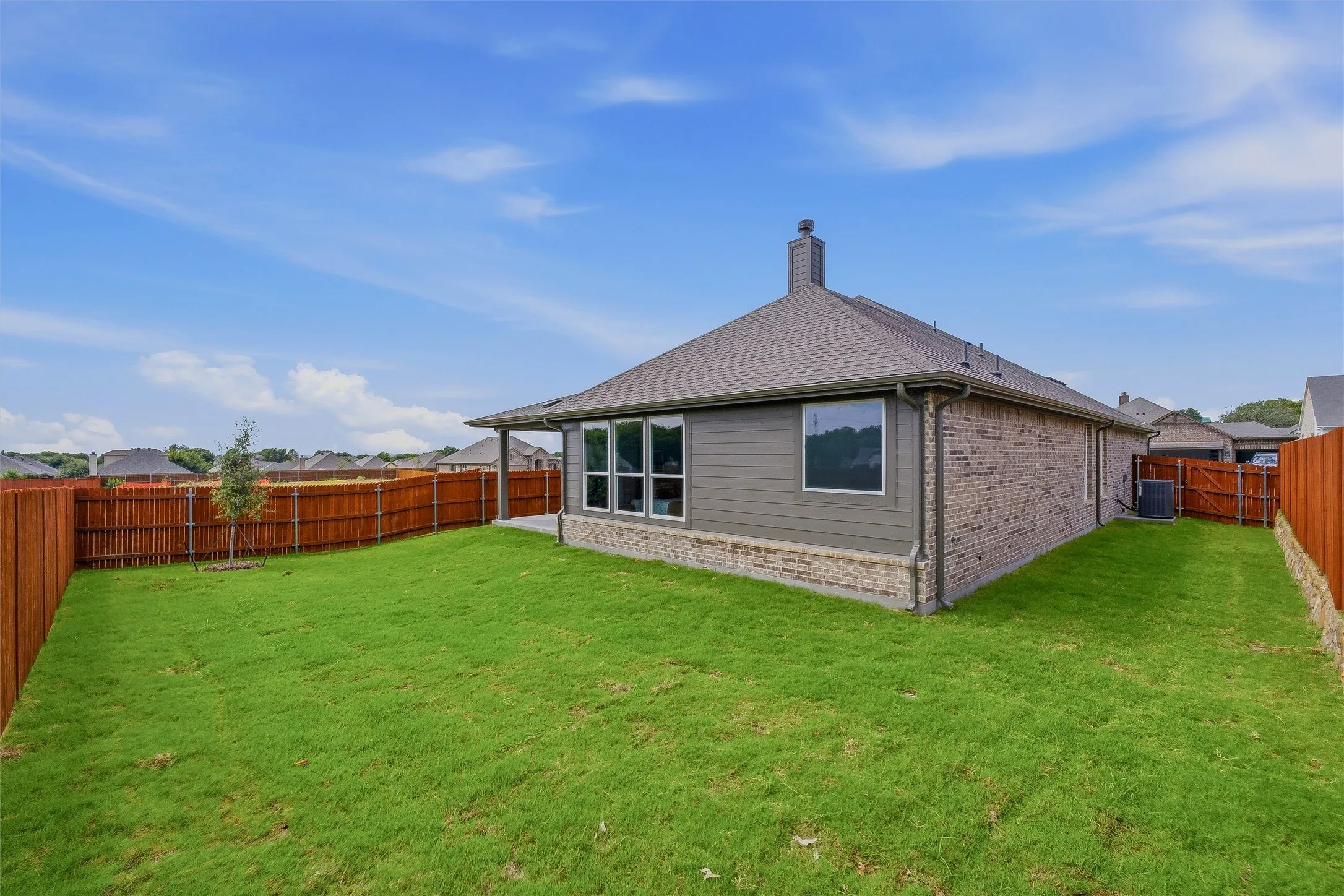 Expansive backyard featuring a manicured lawn, wood fencing, and a covered patio