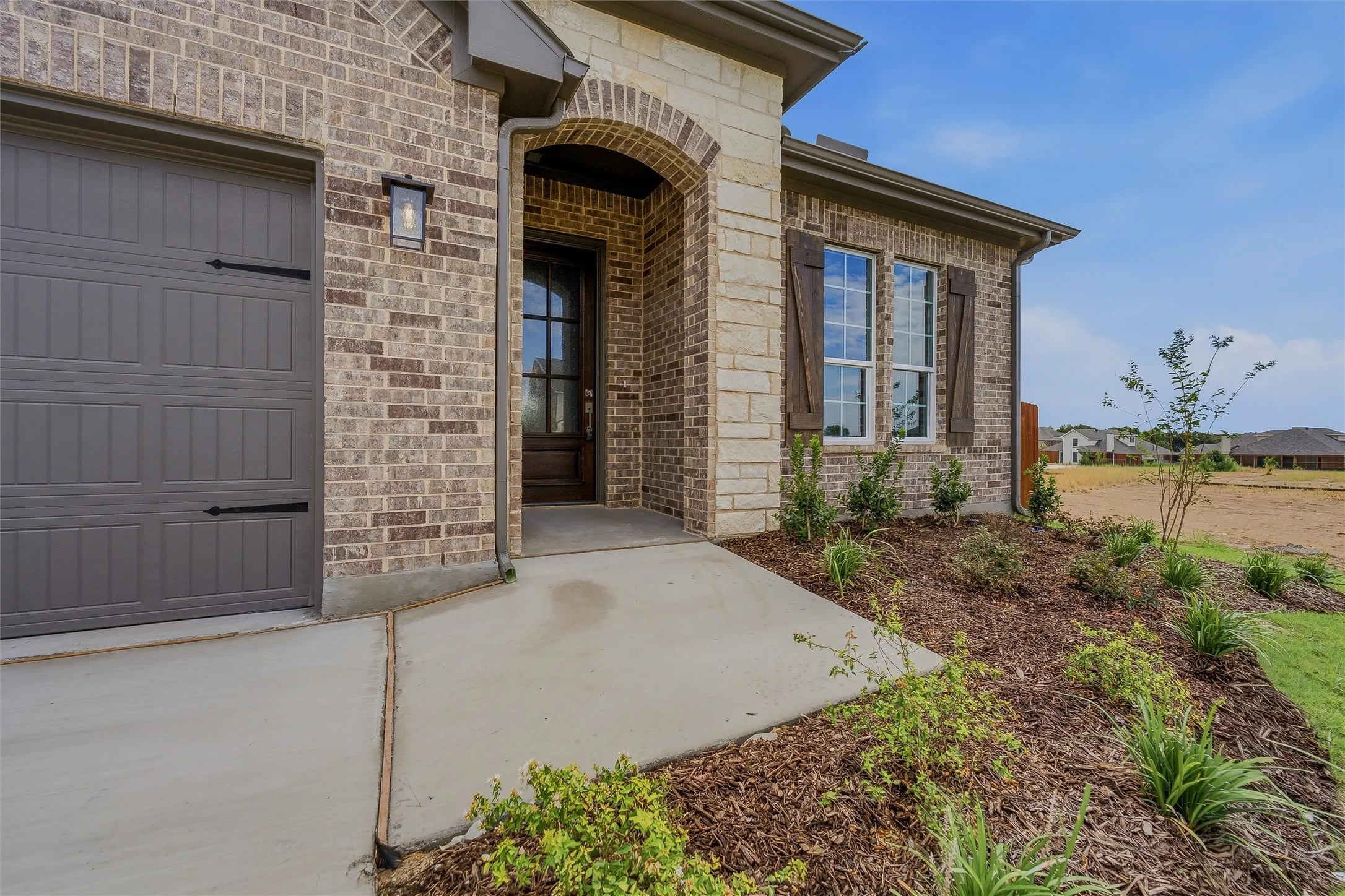 Brick and stone exterior with a paneled garage door and an arched entryway