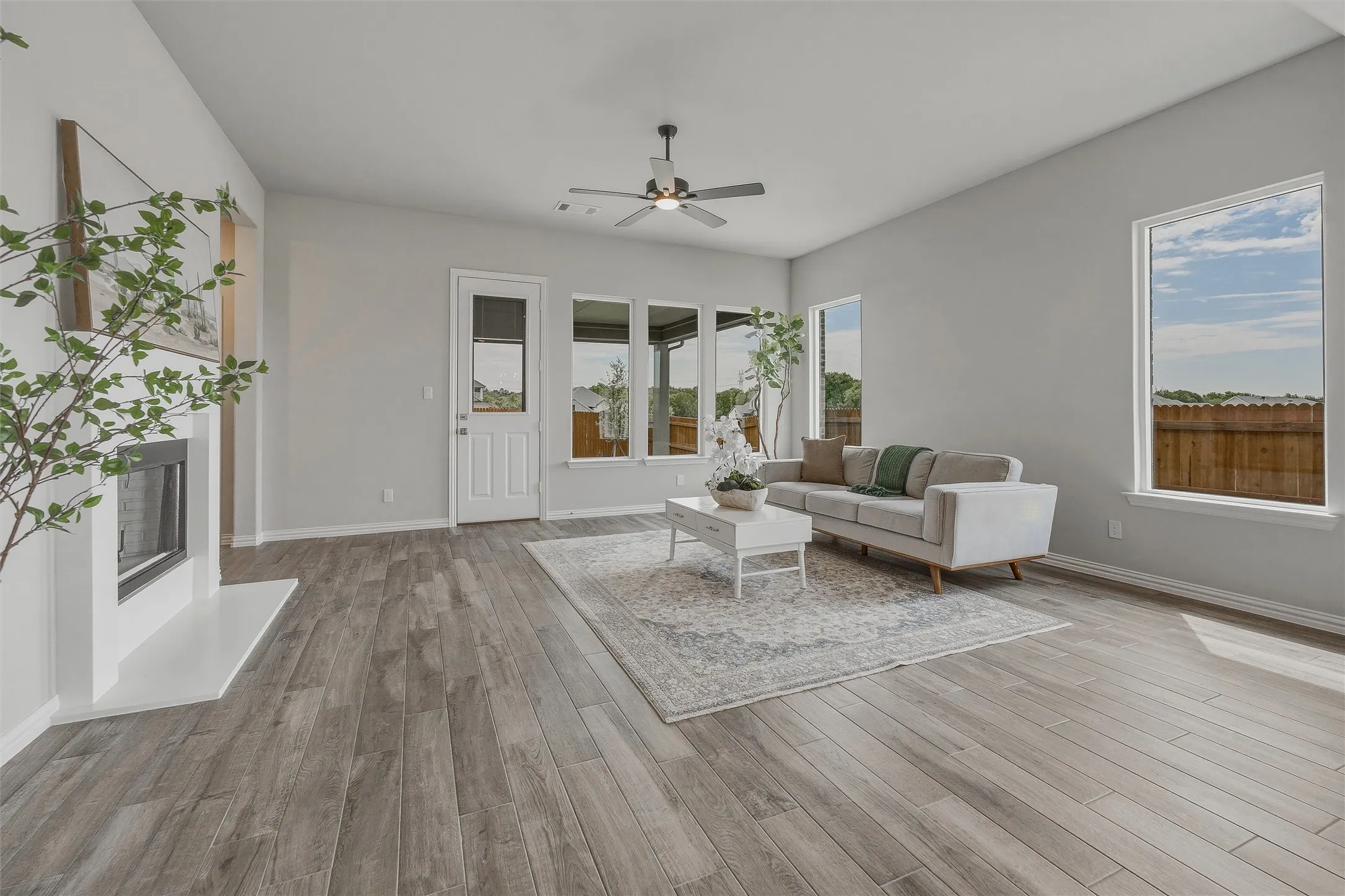 Spacious living area featuring wood-finish flooring, a contemporary fireplace, multiple windows, and a ceiling fan