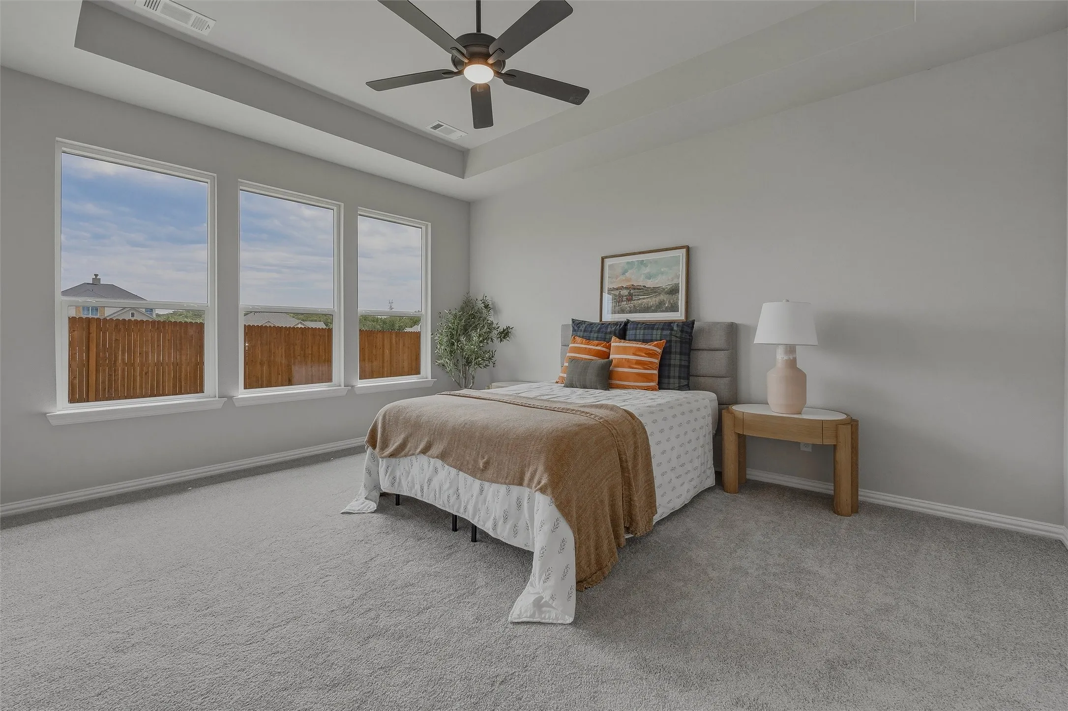 Tray ceiling with recessed lighting, ceiling fan, three large windows, gray wall paint, and gray carpet flooring