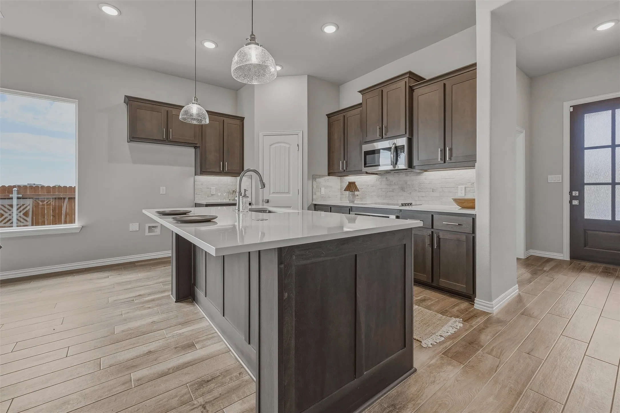 Kitchen featuring a large island with a light-toned countertop, stainless steel appliances, dark wood-finish cabinetry, recessed lighting, and wood-finish flooring