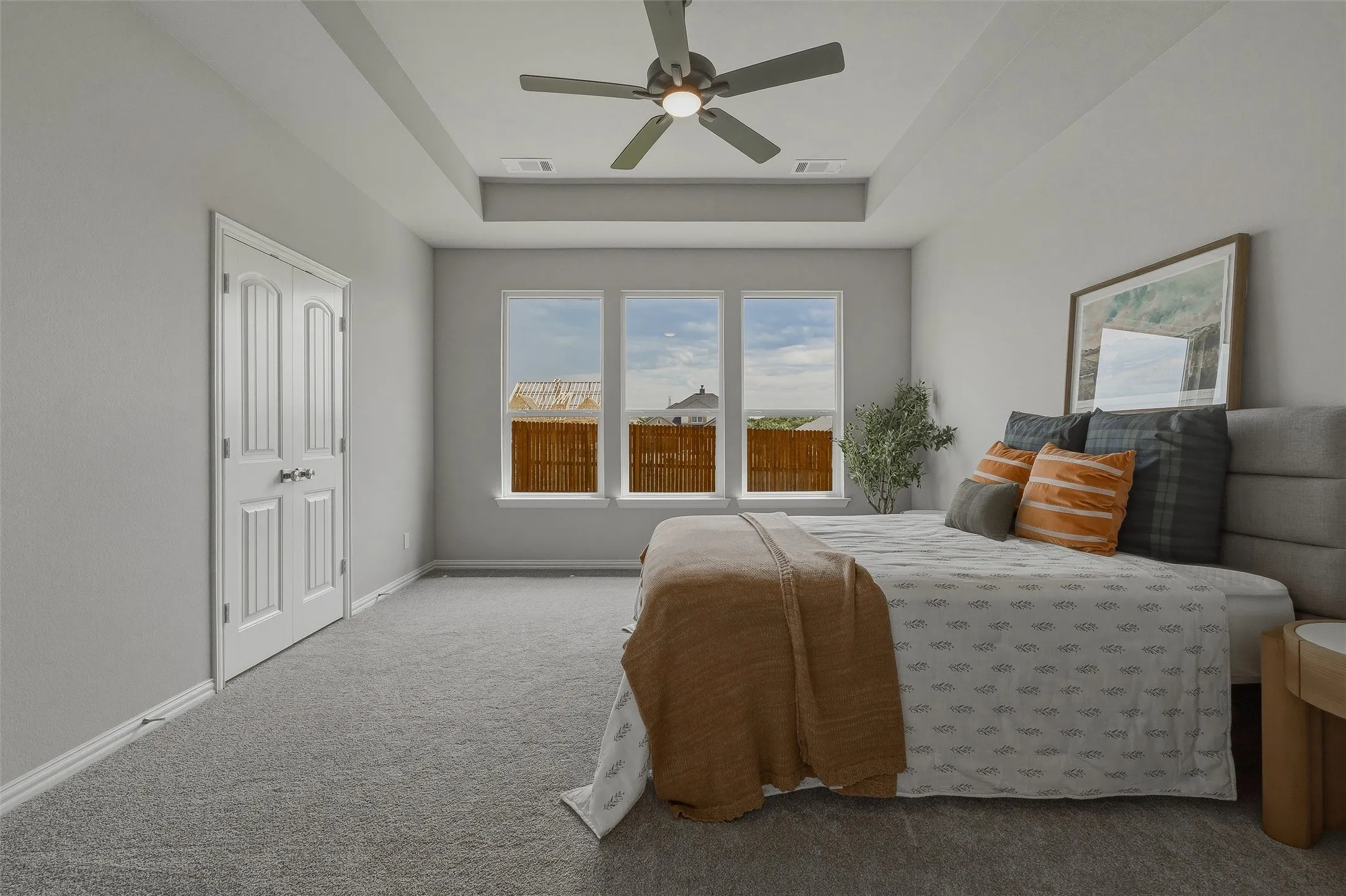 Tray ceiling with a ceiling fan, three paneled windows, double-door closet, and wall-to-wall carpeting
