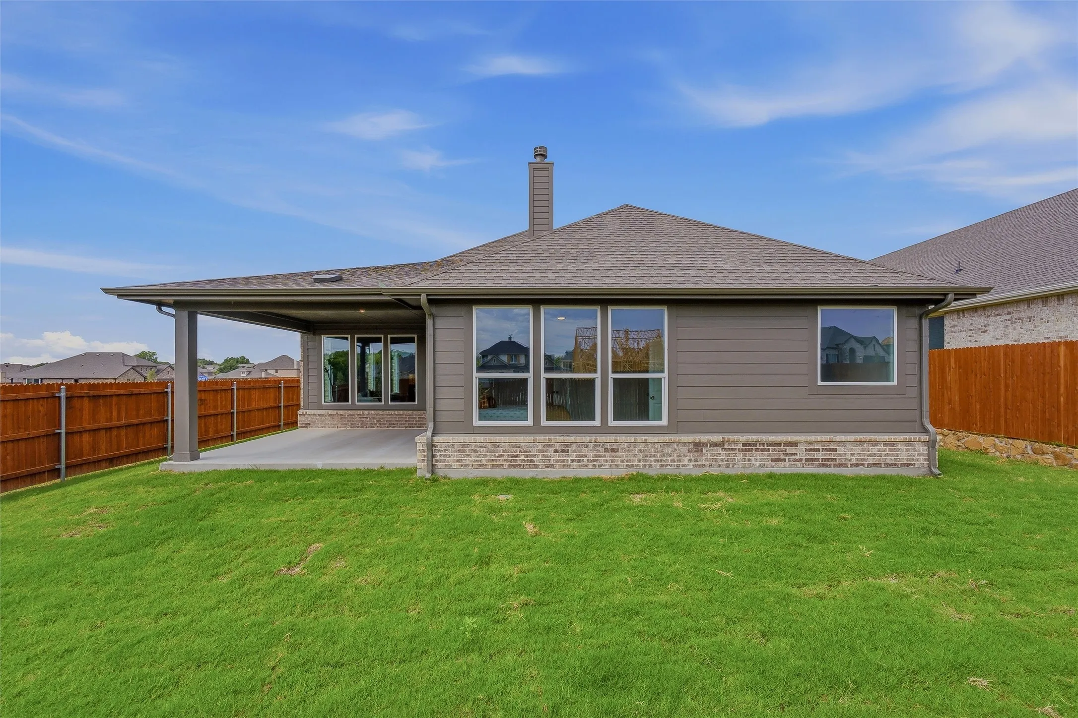 Expansive backyard featuring a covered patio, manicured lawn, full privacy fencing, and brick and siding exterior