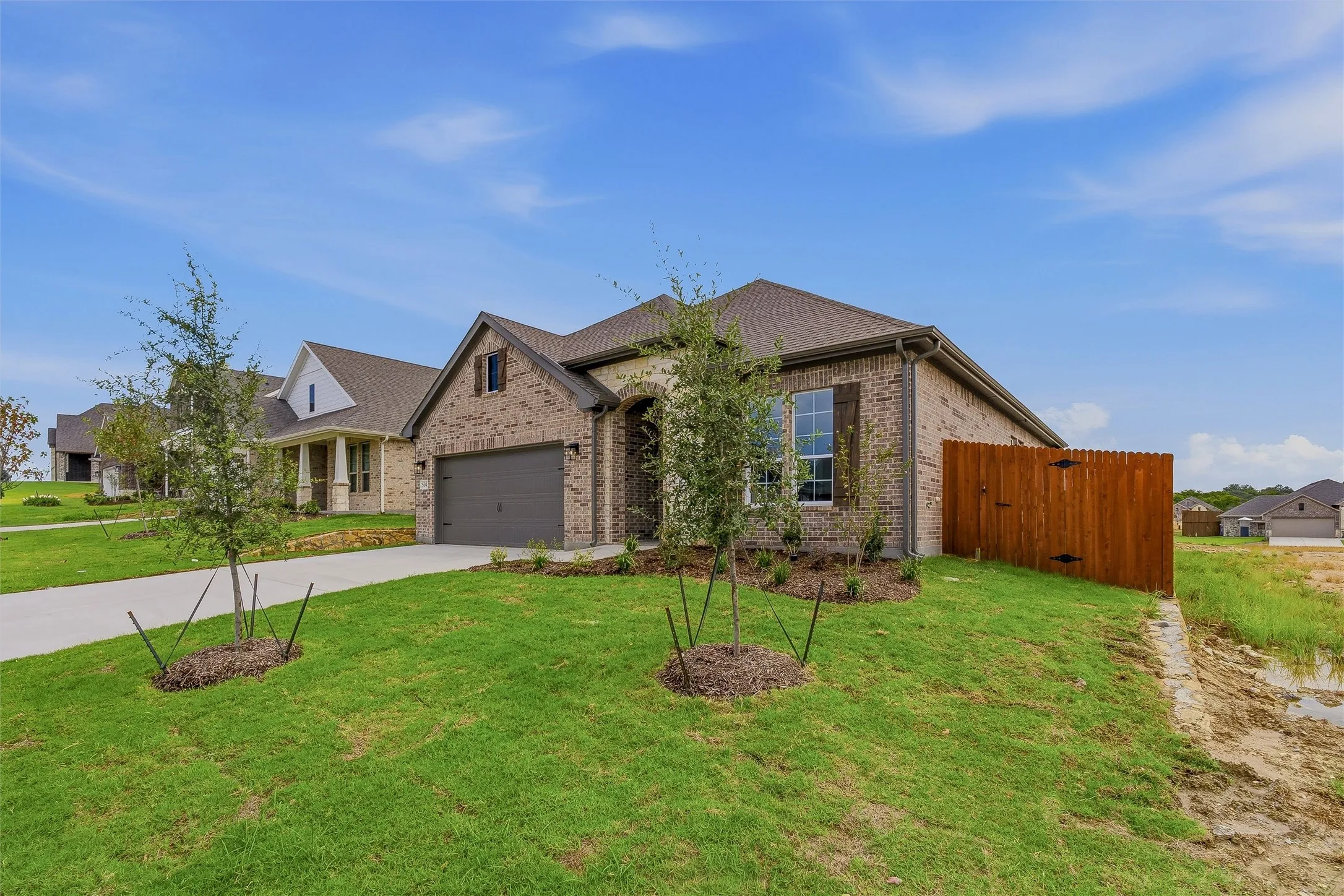 Brick exterior with a dark roof, attached garage, and a wood privacy fence
