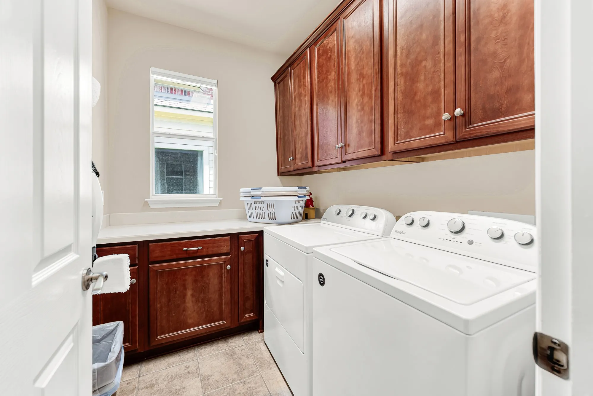 Spacious utility room with abundant upper and lower cabinetry, generous folding counter space, and a window that brings in natural light—making everyday chores more convenient and organized.