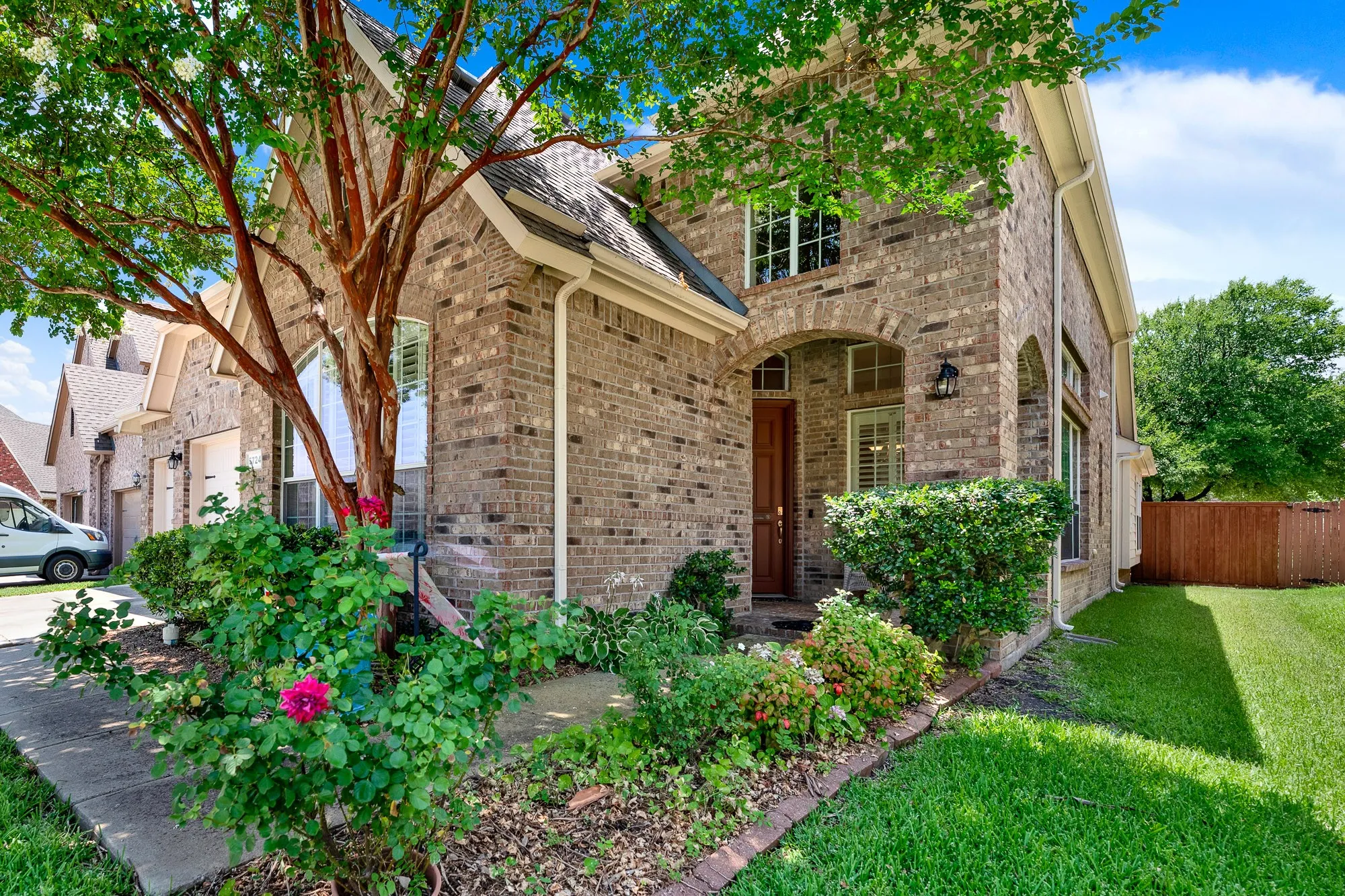 The welcoming covered front porch is framed by lush landscaping and flowering crepe myrtles, offering a warm first impression and inviting entry into this beautifully maintained home.