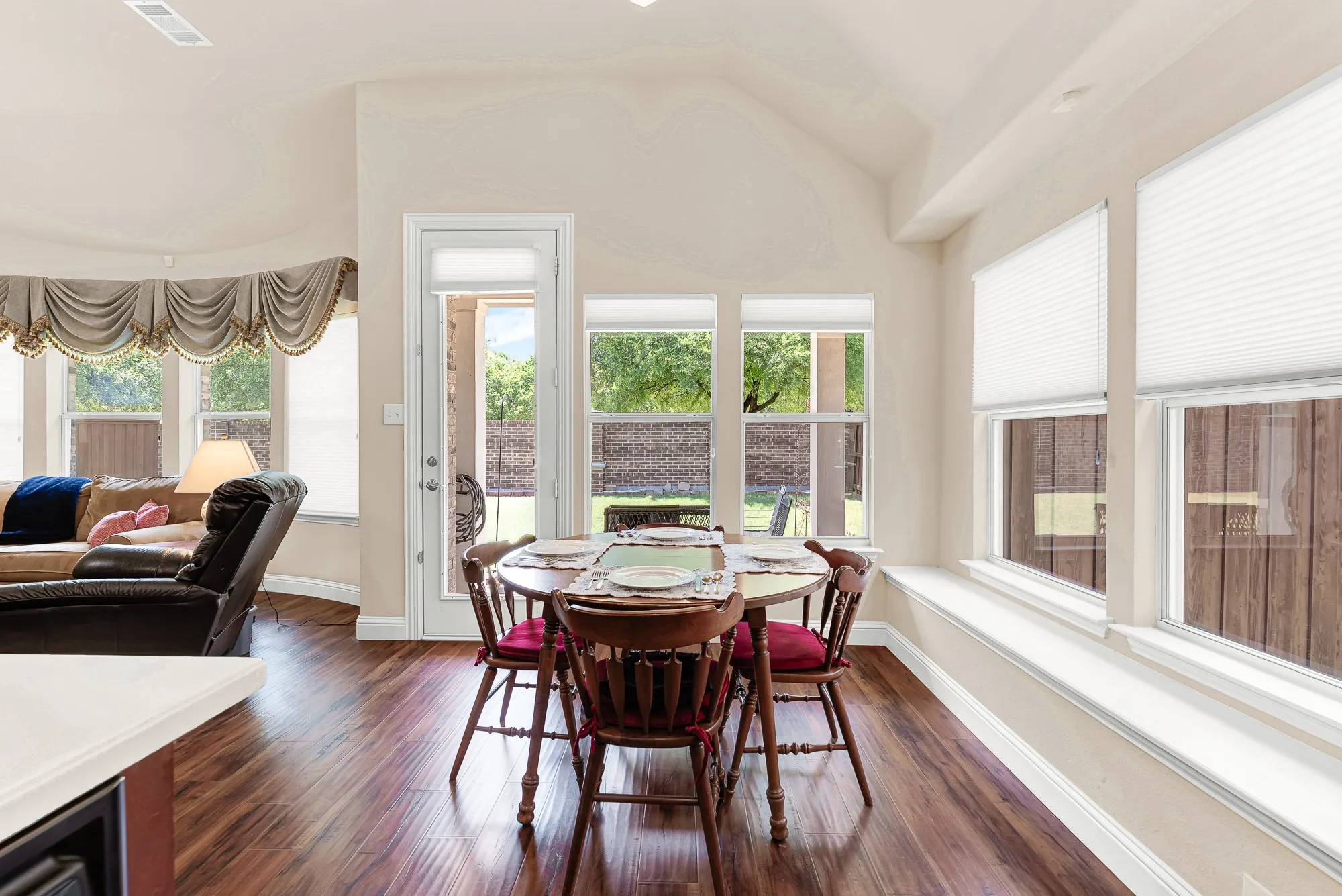 The sunlit breakfast nook is surrounded by windows, creating the perfect spot to enjoy your morning coffee while taking in peaceful views of the backyard. A glass door provides easy access to the covered patio.