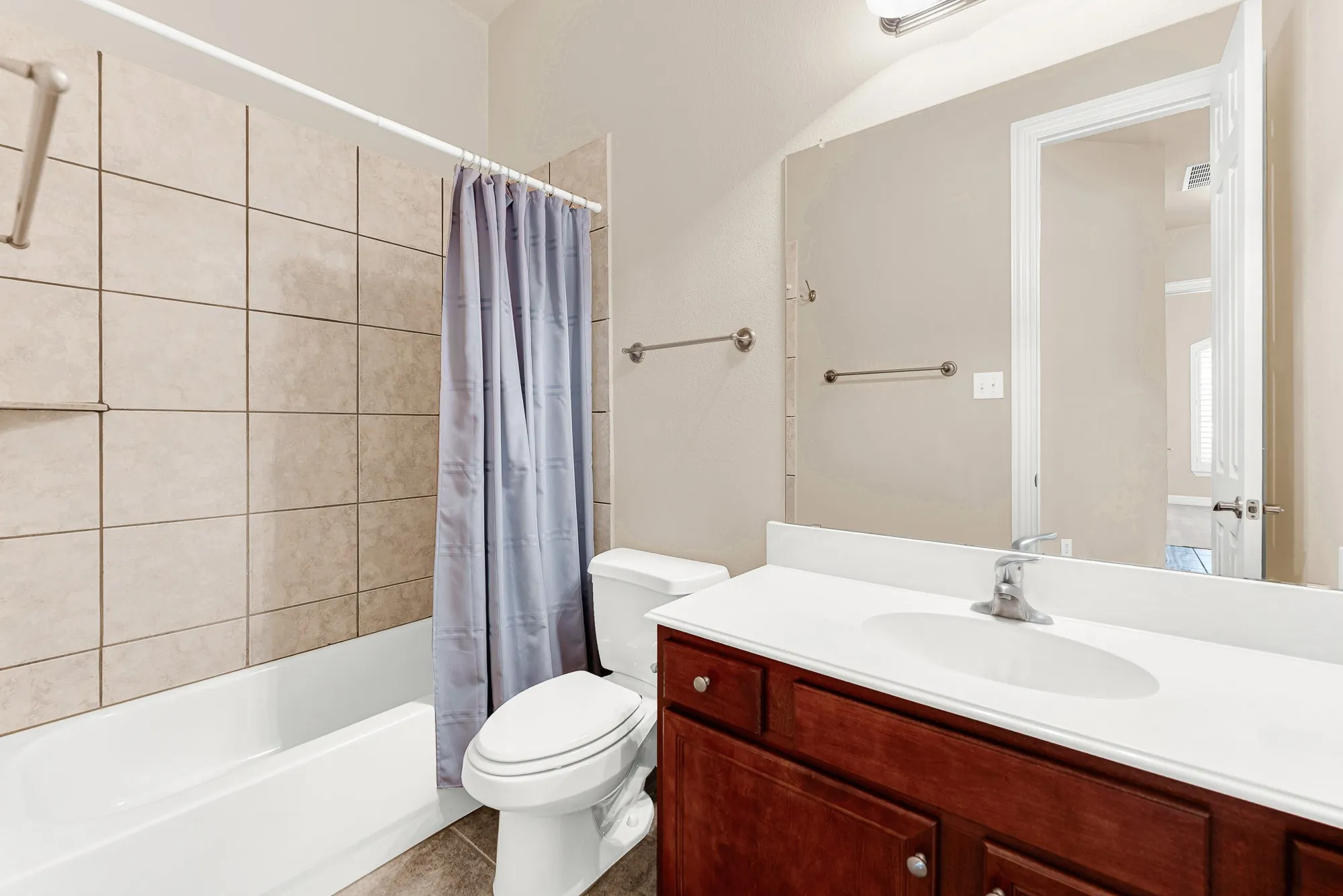 Convenient full bathroom featuring a tiled tub/shower combination, oversized vanity with ample storage, and a large mirror.
