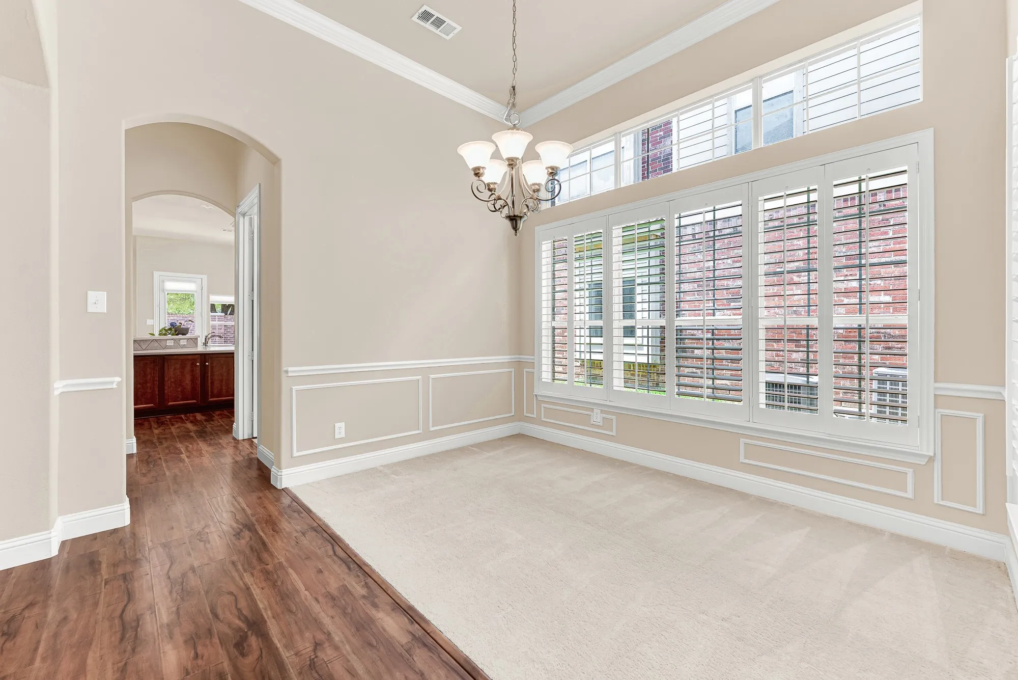 Elegant formal dining room featuring crown molding, decorative wall trim, soaring ceilings, and plantation shutters that fill the space with beautiful natural light.