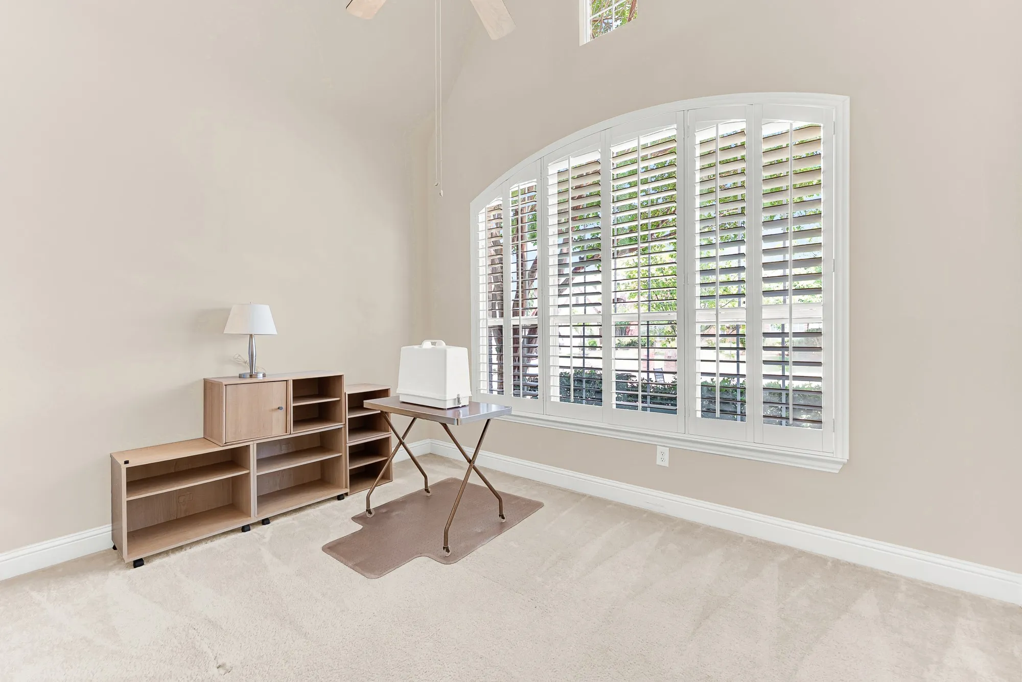 Spacious secondary bedroom with soaring ceilings, an oversized arched window with plantation shutters, and abundant natural light—perfect as a guest room, home office, or hobby space.