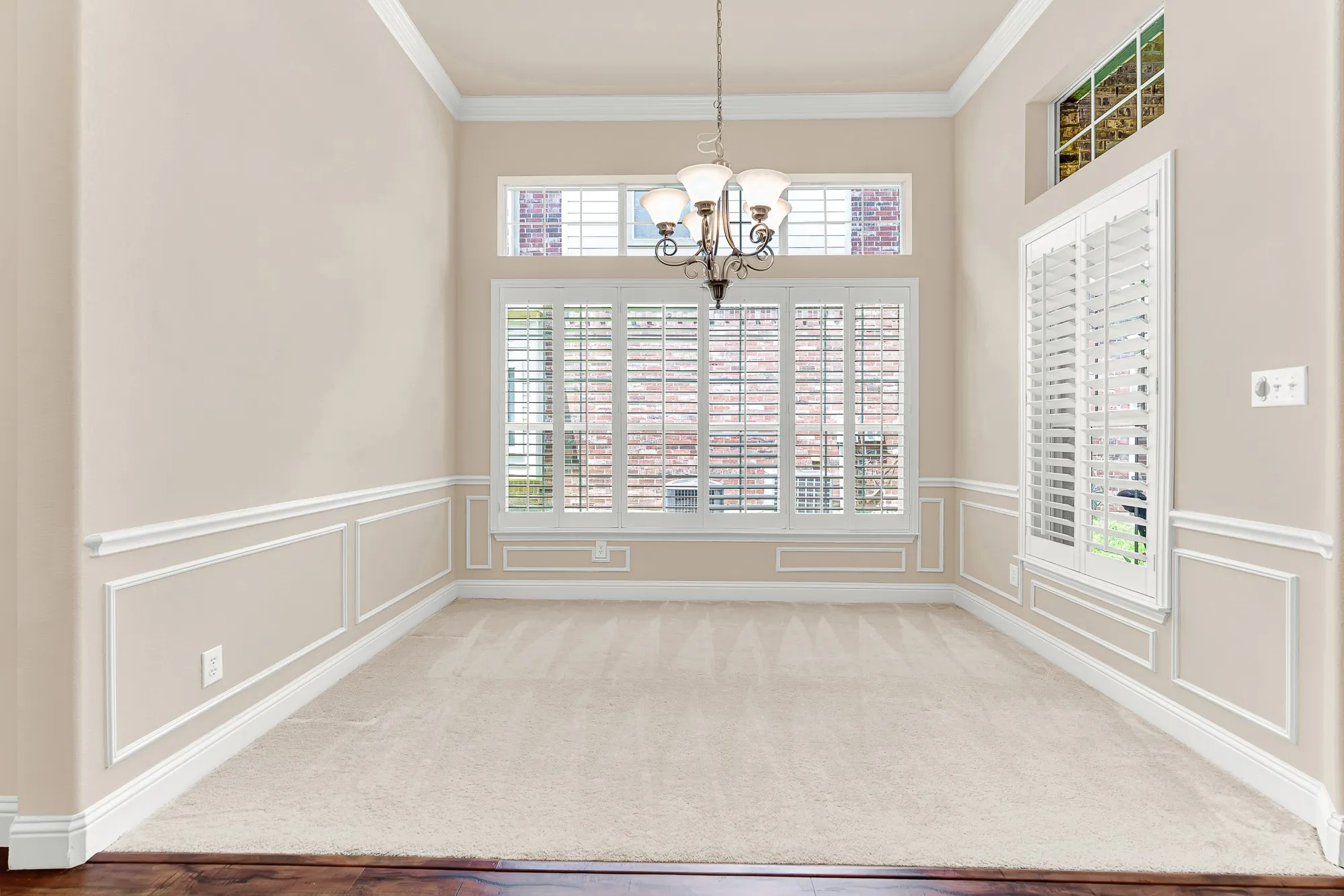The dedicated dining room offers timeless architectural details, including extensive molding, a classic chandelier, and oversized windows with plantation shutters for an inviting atmosphere.