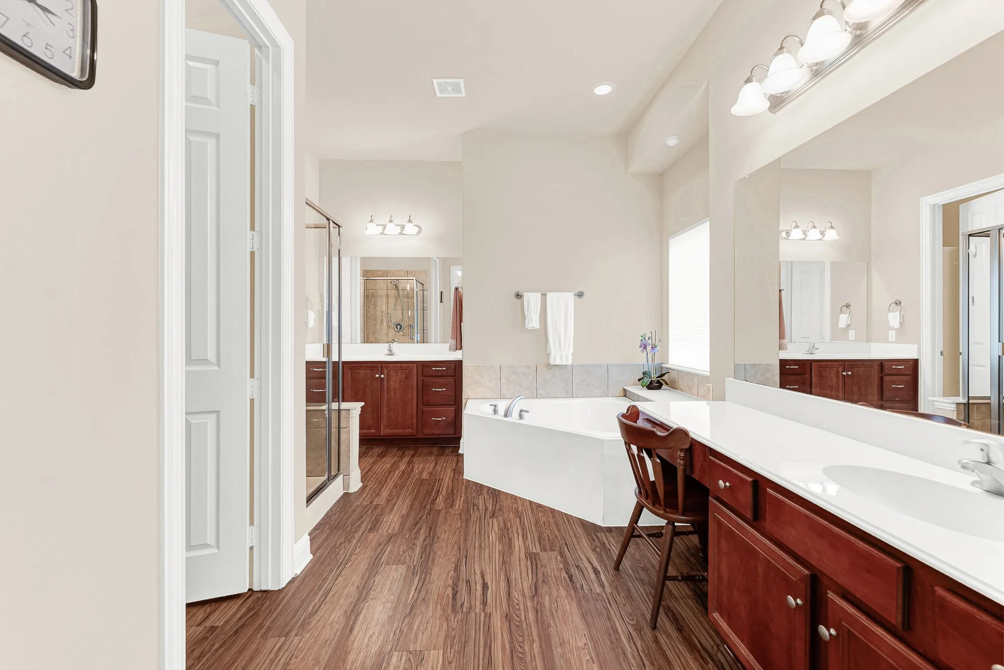 The spacious primary bath features separate vanities, a dedicated makeup vanity, a relaxing corner soaking tub, and plenty of storage, creating a functional everyday retreat.