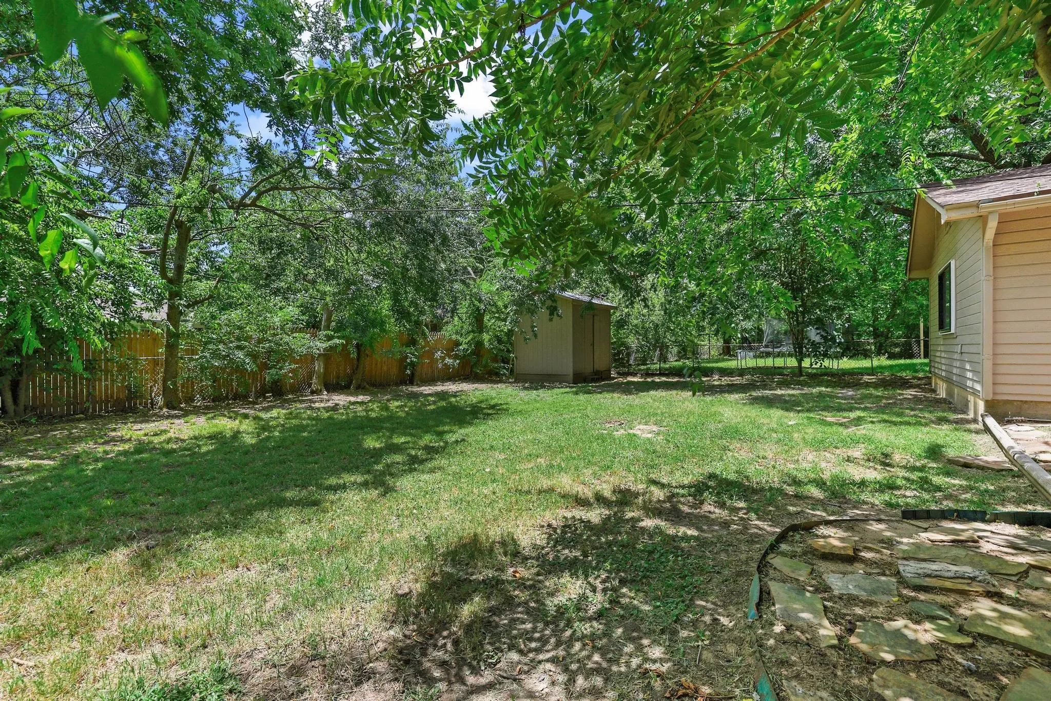 Expansive lawn area featuring mature trees and a wood privacy fence