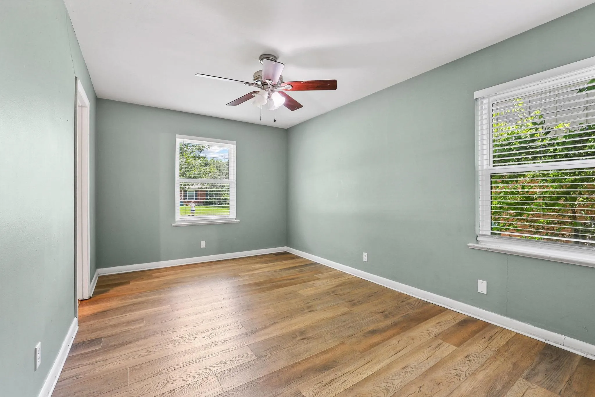 Room featuring wood-finish flooring, two windows with blinds, a ceiling fan, and light-colored walls