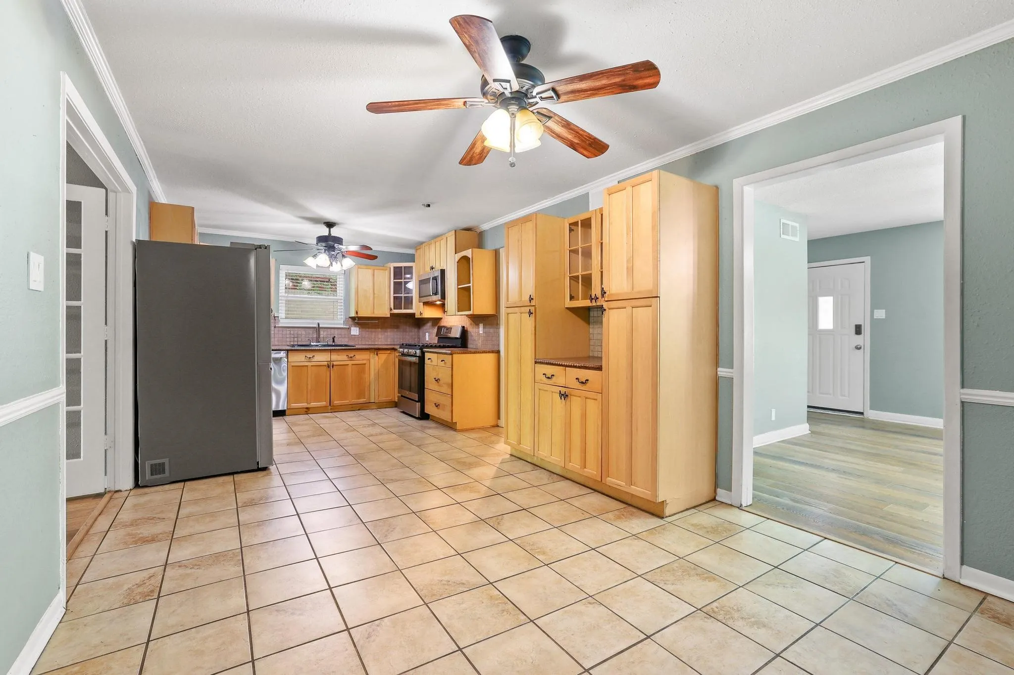 Kitchen featuring tile flooring, light wood cabinetry, a dark finished refrigerator, and a ceiling fan