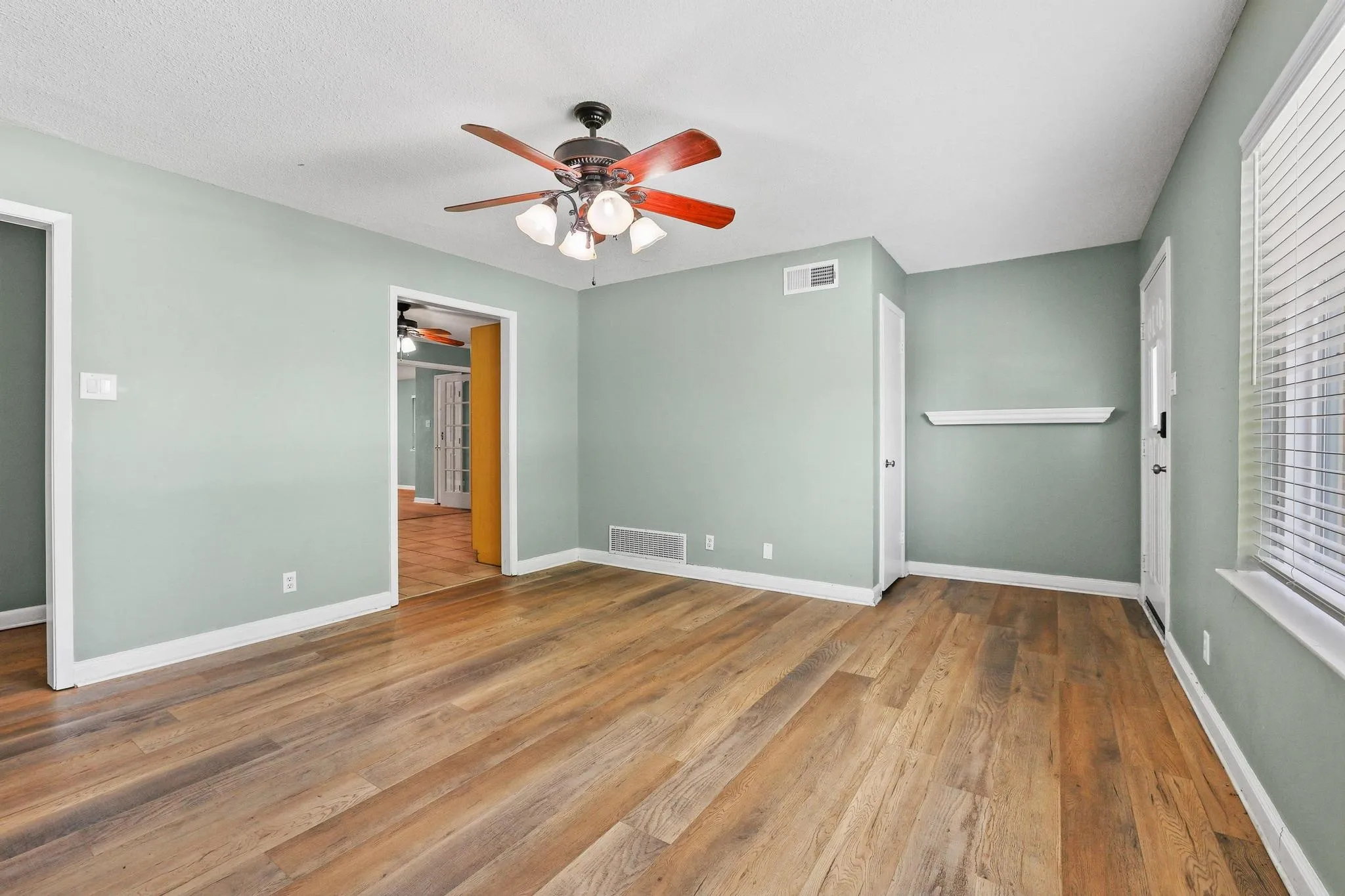 Spacious room featuring wood-finish flooring, light green walls, and white trim