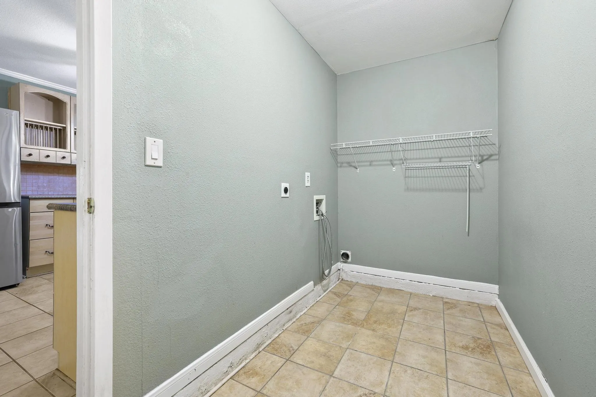 Utility area featuring neutral-toned tile flooring, light gray walls, and an integrated wire shelving system