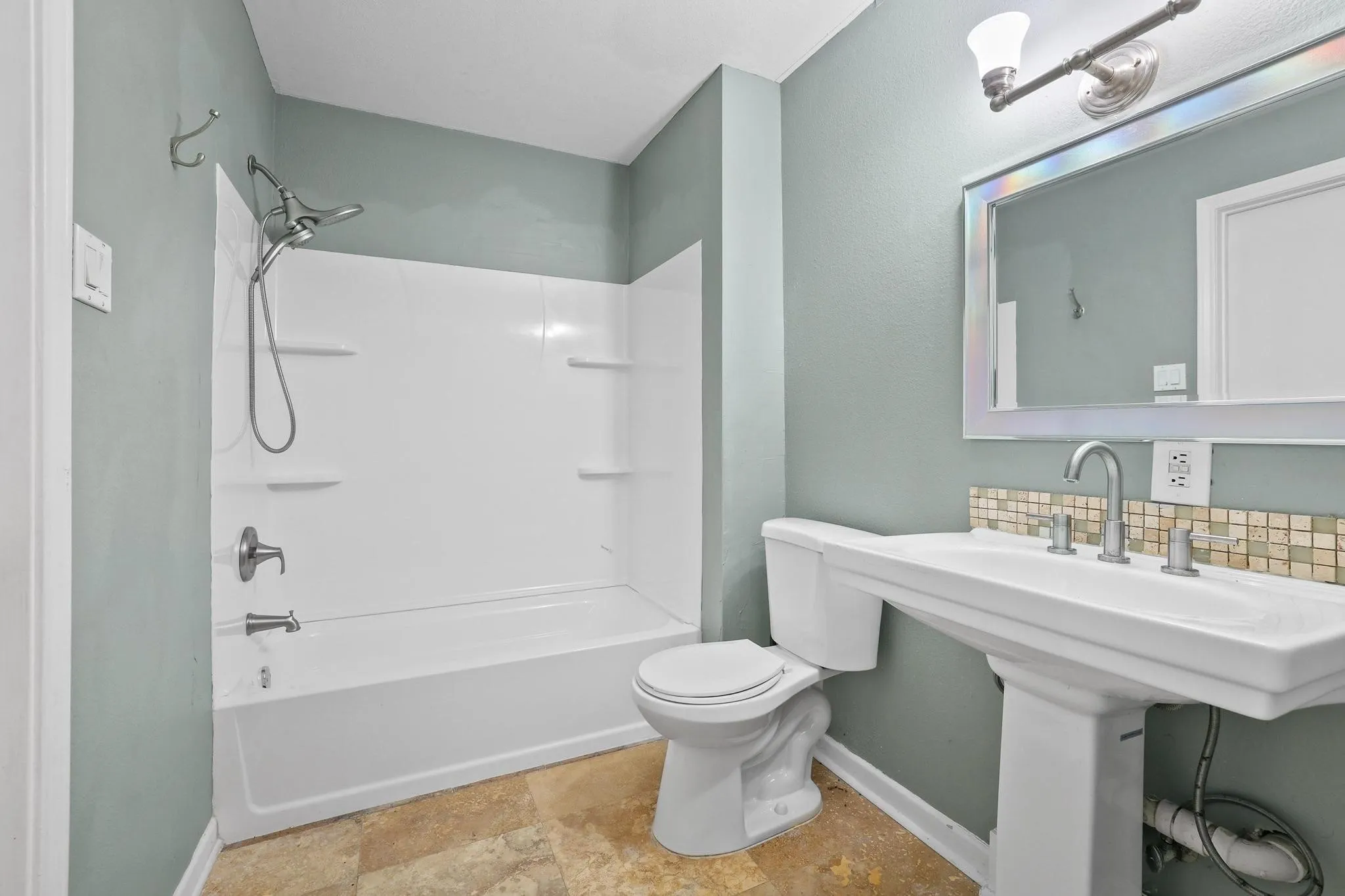 Bathroom featuring a white pedestal sink, vanity mirror with overhead lighting, and a neutral tile backsplash