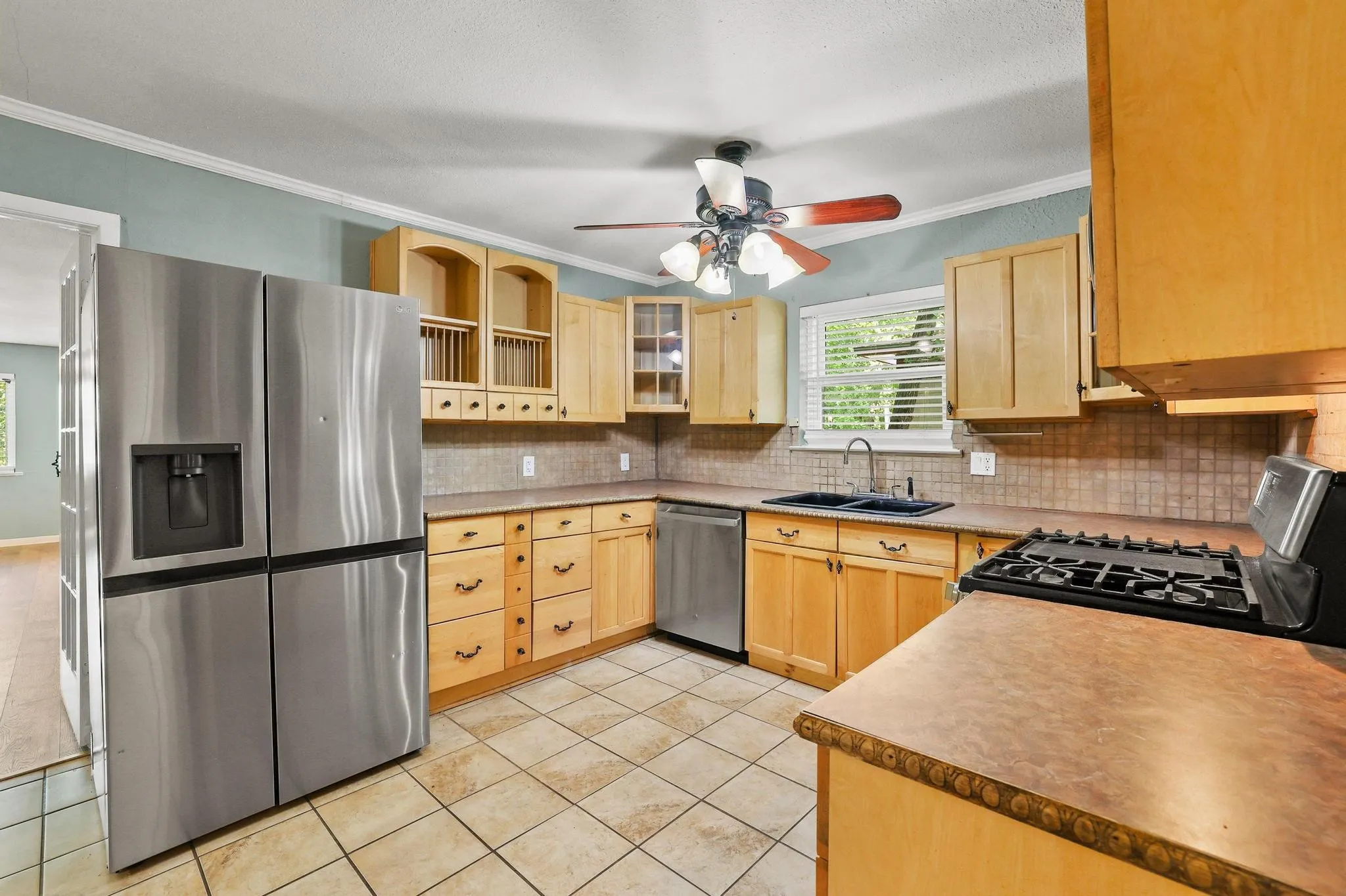 Kitchen featuring stainless steel appliances, wood-finish cabinetry, tile flooring, a gas range, and a ceiling fan with integrated lighting