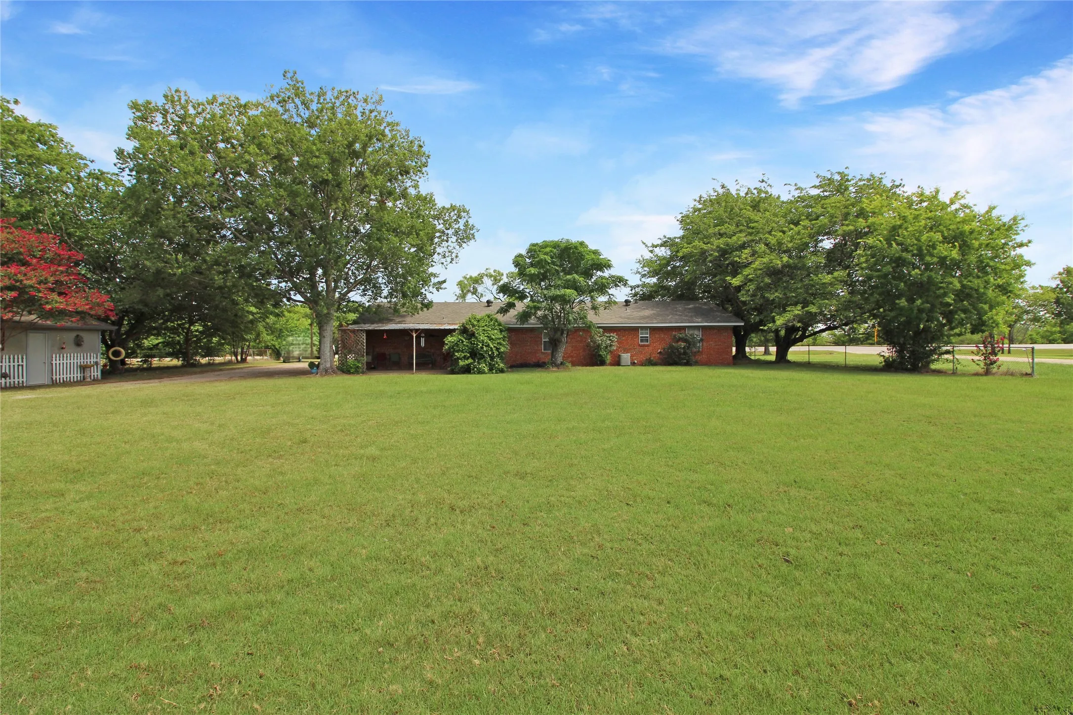 Expansive green lawn with mature trees and a brick-sided residence