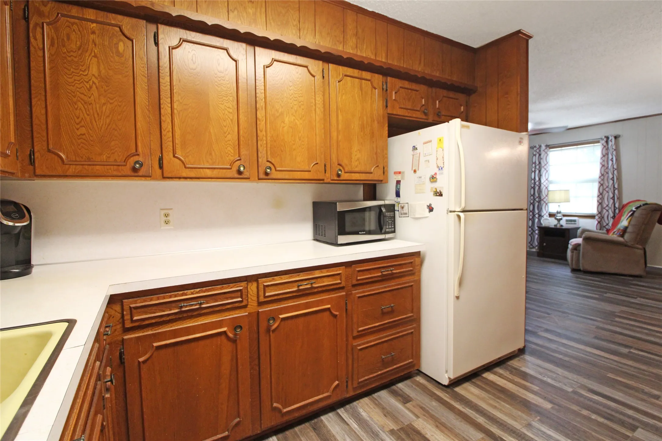 Kitchen featuring wood cabinetry, white countertops, a built-in refrigerator alcove, and wood-finish flooring extending into the adjacent living space