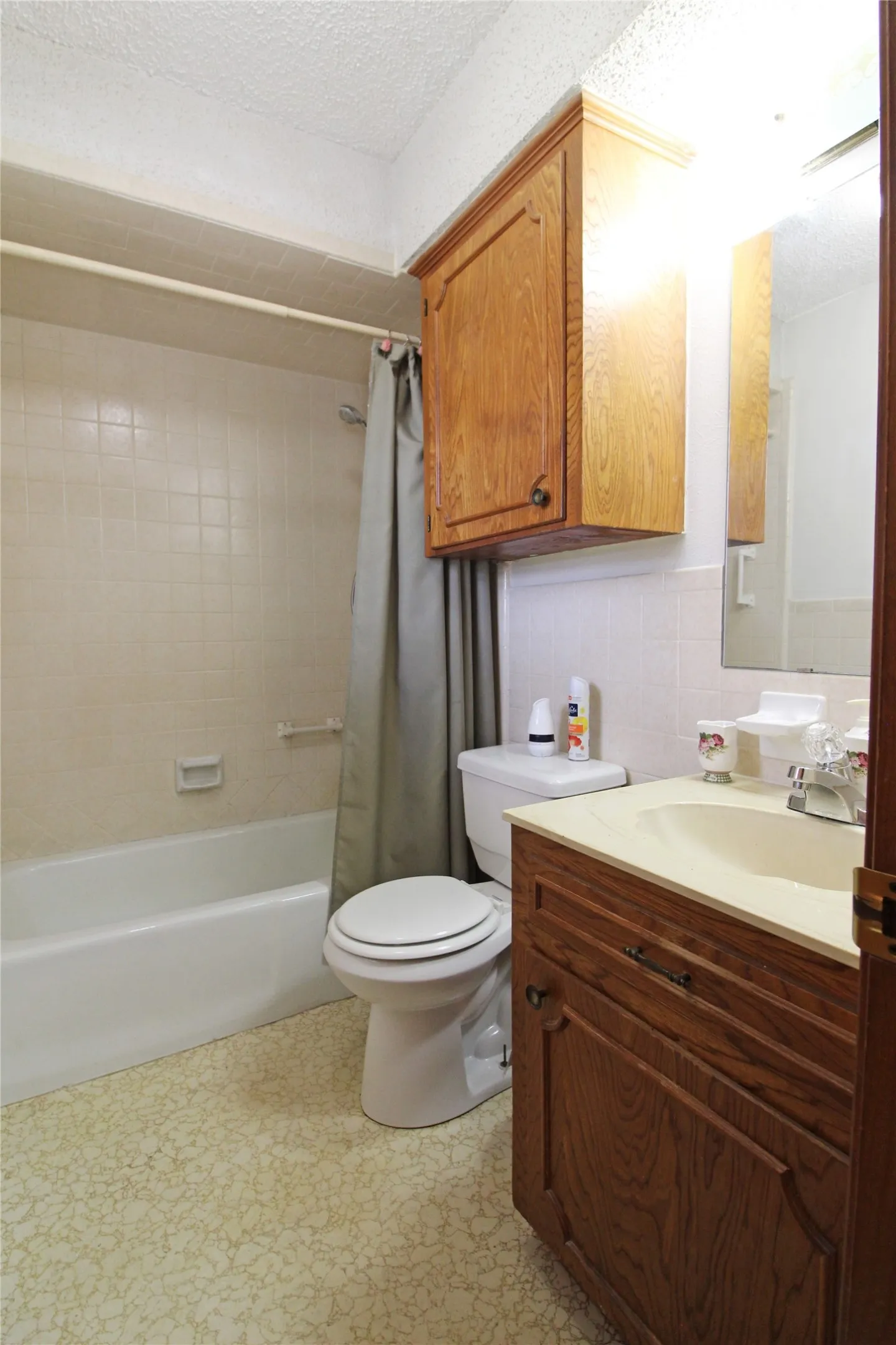 Bathroom featuring a built-in bathtub with tiled surround, a white toilet, and a vanity with wood-finish cabinetry and a light-colored countertop with an integrated sink