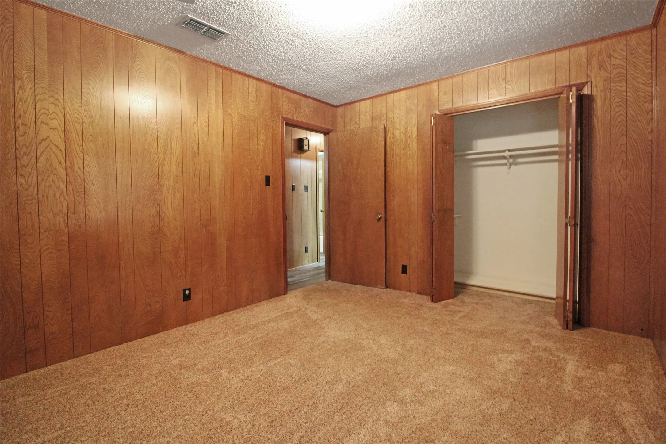 Room with wood paneling, plush carpeting, and a built-in closet with double bi-fold doors
