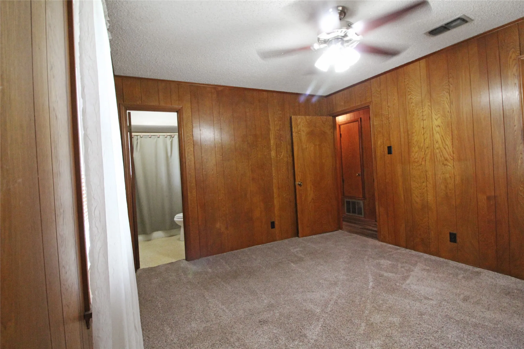 Interior room featuring wood paneling walls, a ceiling fan with light fixture, and textured carpet flooring