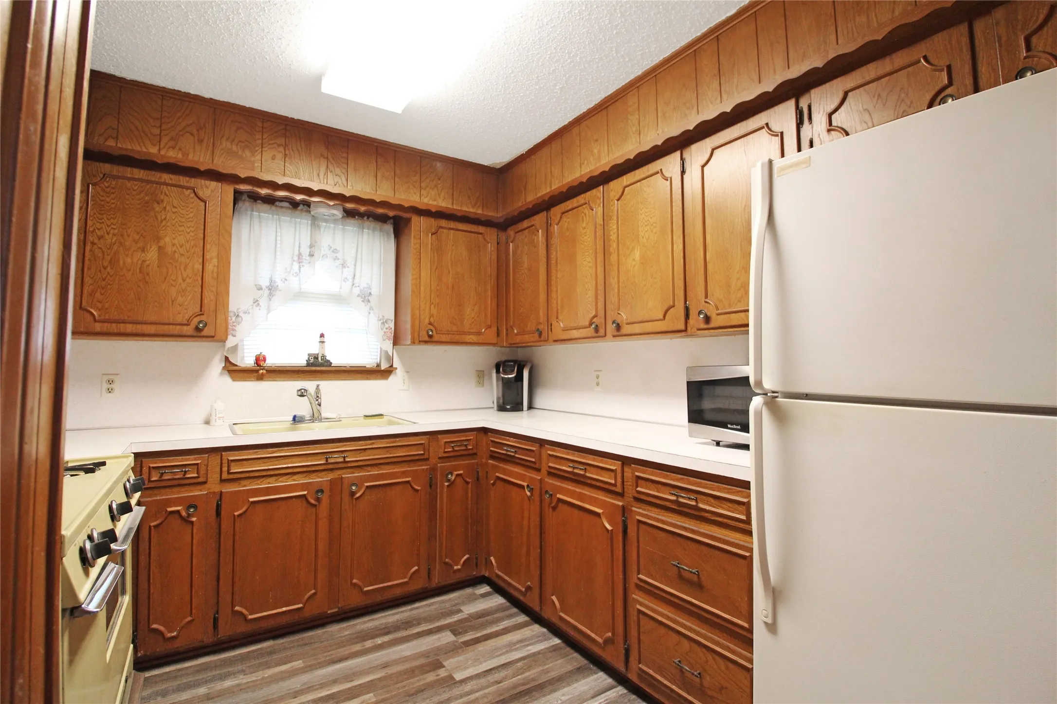 Kitchen featuring wood cabinetry, white countertops, a double-basin sink, and wood-finish flooring