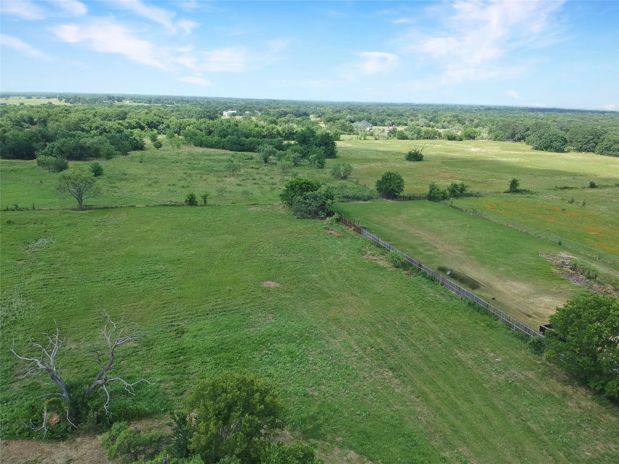 Expansive green pastures featuring mature trees and a partial fence line