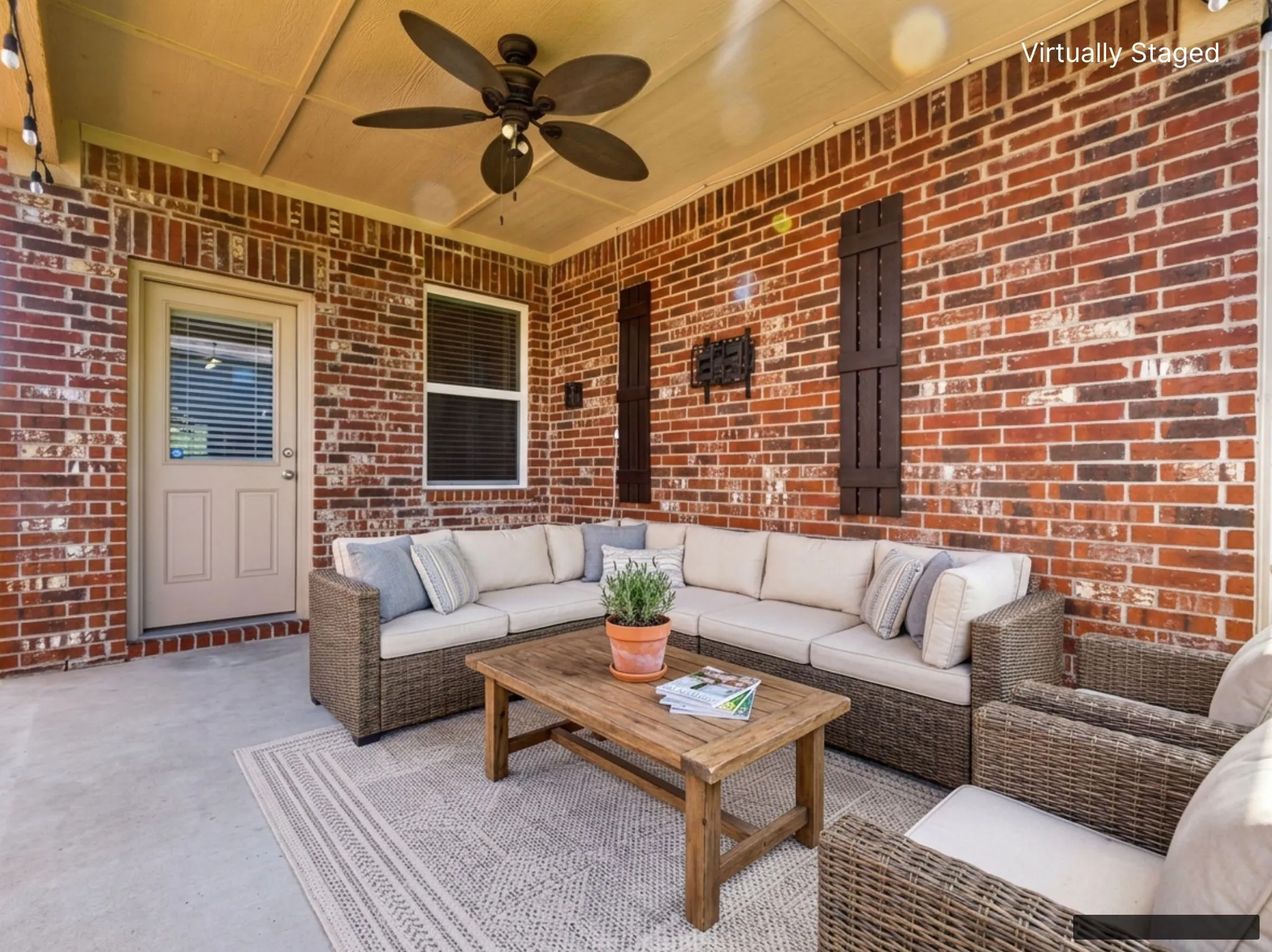 Covered outdoor patio featuring a brick exterior wall and a ceiling fan