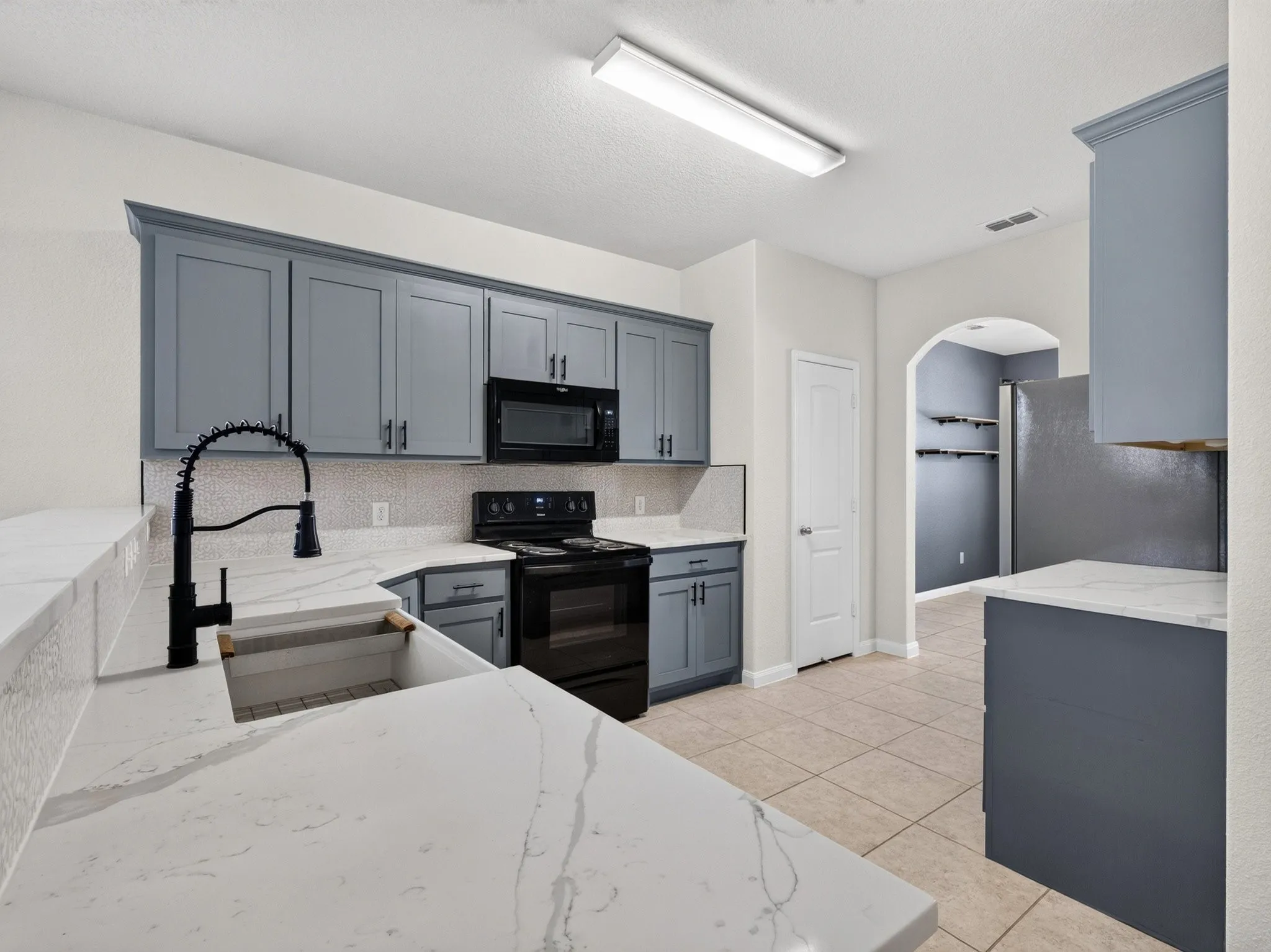 Kitchen featuring light gray cabinetry, white countertops, black appliances, a white tile backsplash, and tile flooring
