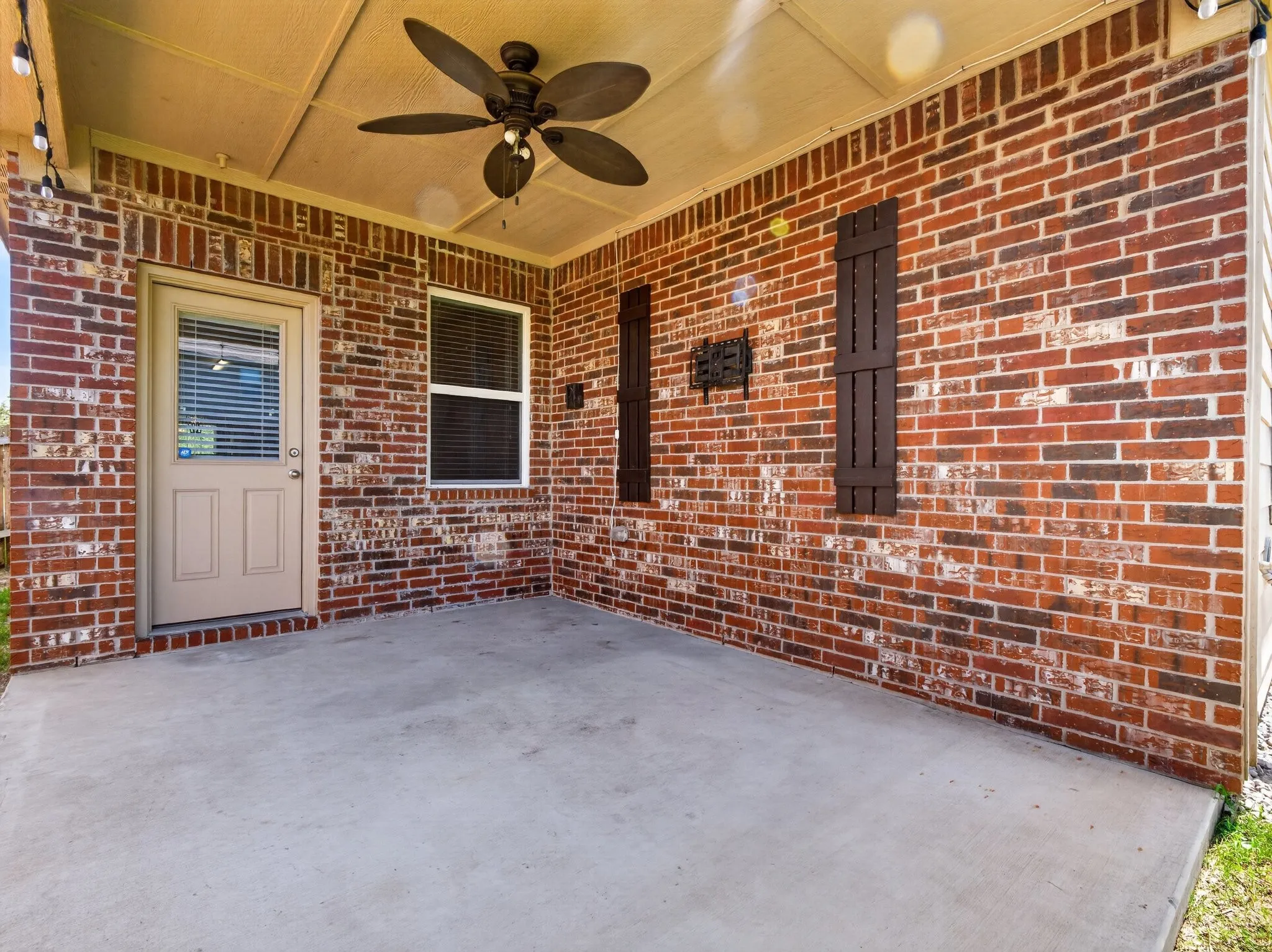 Covered patio featuring a ceiling fan, string lighting, and red brick exterior