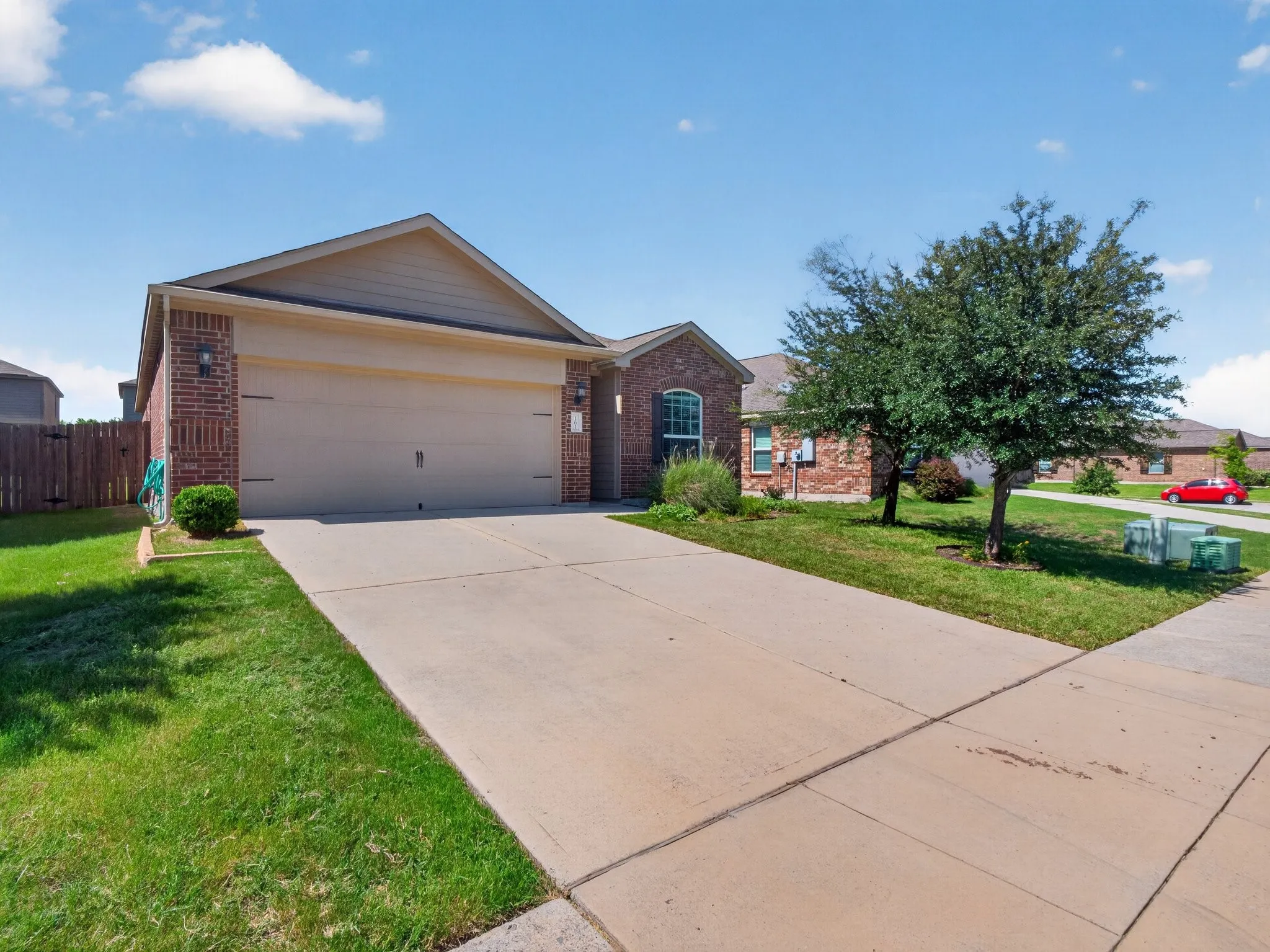 Brick and siding exterior featuring an attached two-car garage, concrete driveway, and front lawn with mature trees