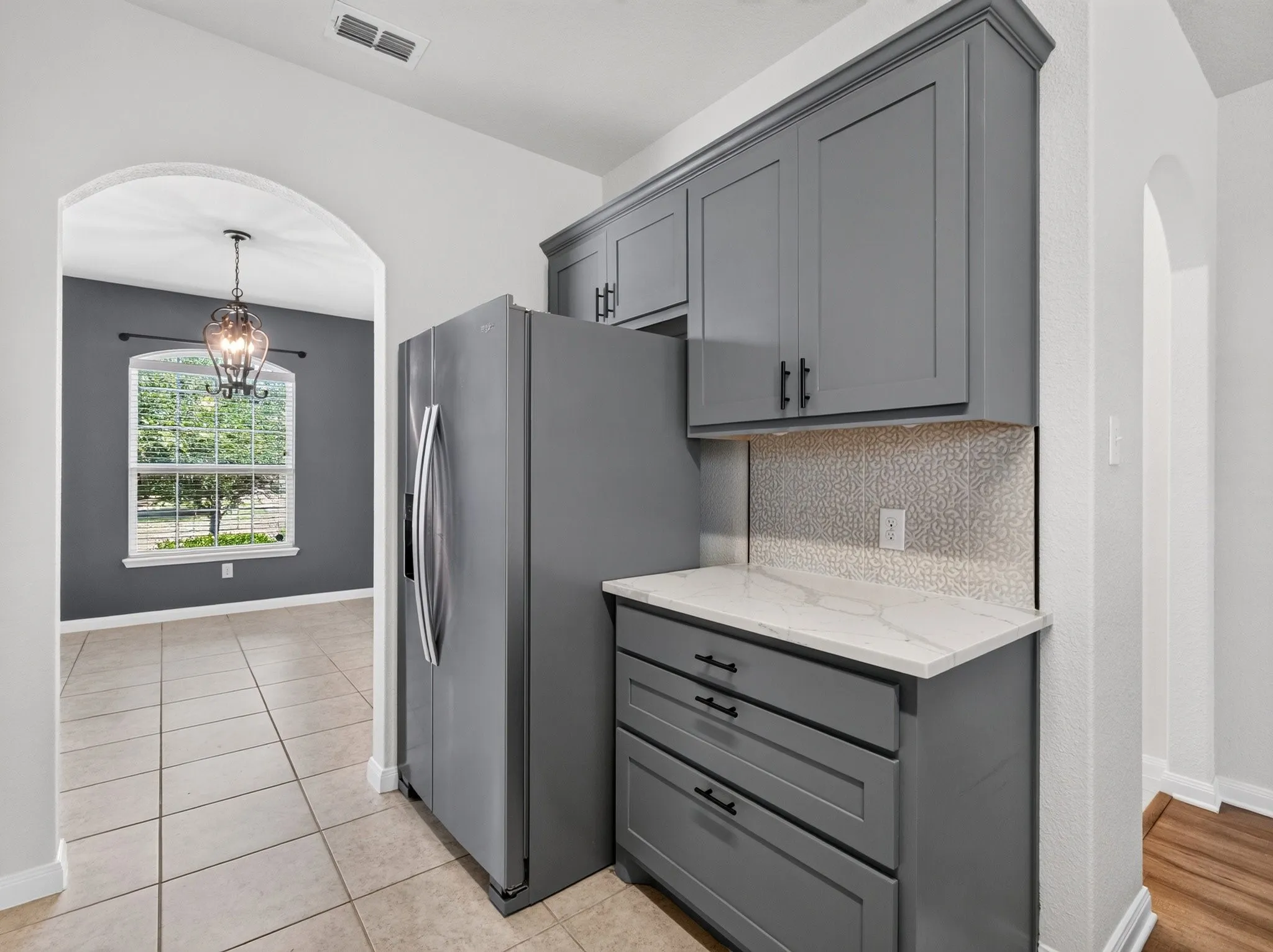 Contemporary kitchen cabinetry in a gray finish with black hardware, featuring a white countertop and a textured backsplash