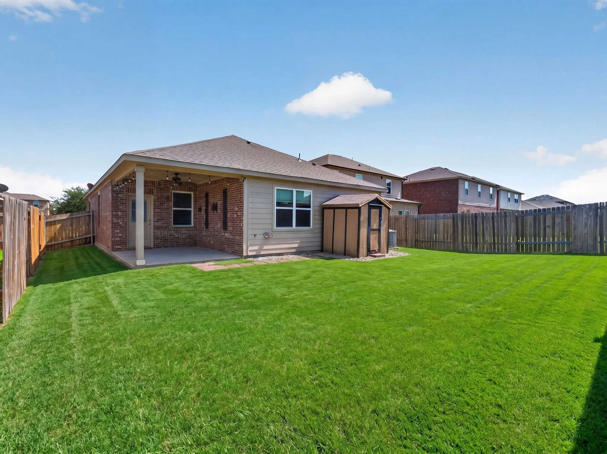 Expansive green lawn with a covered patio, brick exterior, and full perimeter wood fencing