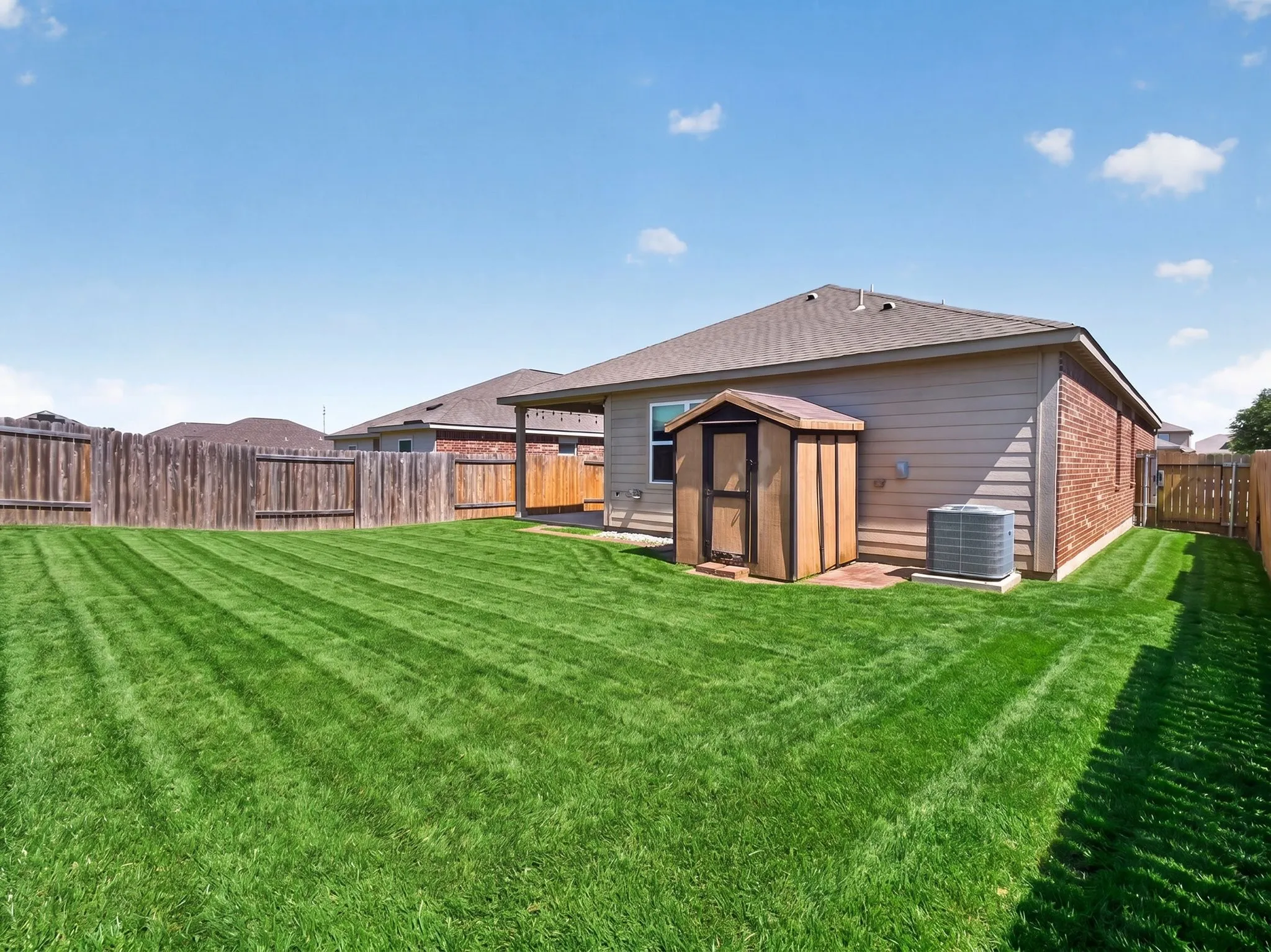 Expansive backyard featuring a manicured lawn, full wood privacy fencing, and a compact storage shed