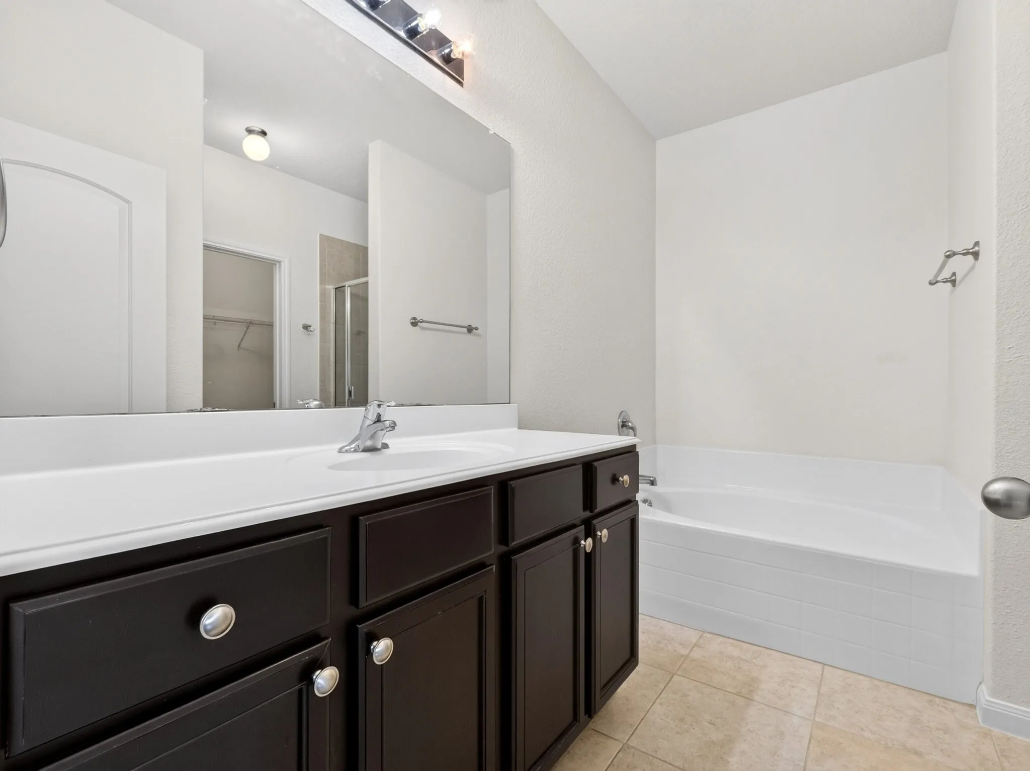 Bathroom featuring a double vanity with dark wood cabinetry, a white countertop, and a built-in bathtub with white tile surround