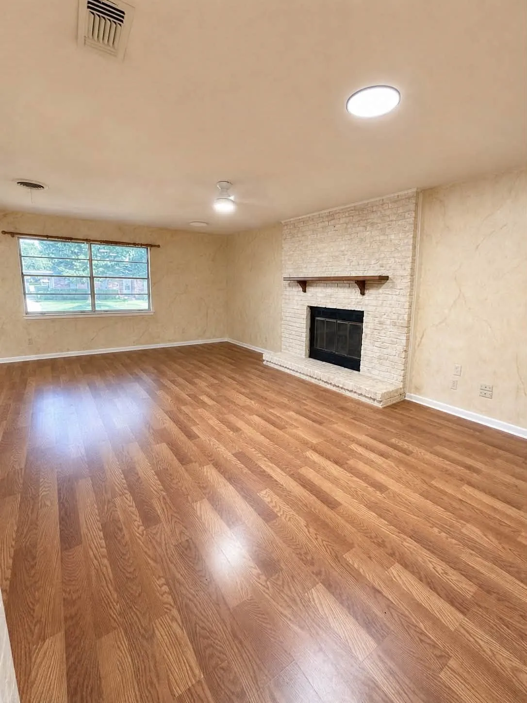 Spacious room featuring wood-finish flooring, a brick fireplace with a wood mantle, and a ceiling fan