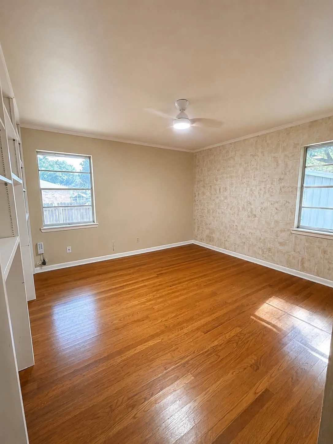Room with wood-finish flooring, two windows, built-in shelving, a ceiling fan with integrated lighting, and crown molding